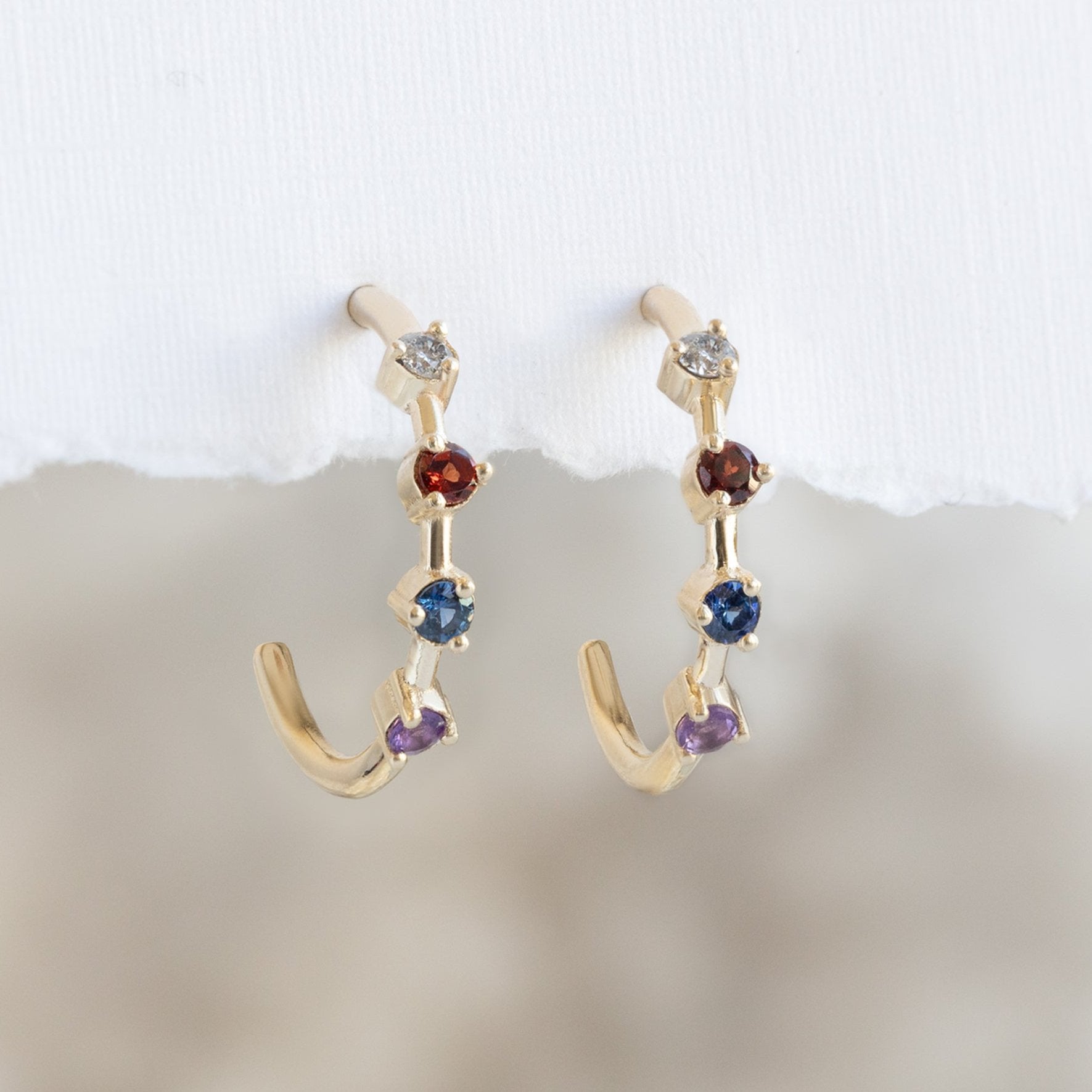 The Custom Multi-Birthstone Hoops 4 Stone Option Hanging on White Textured Paper