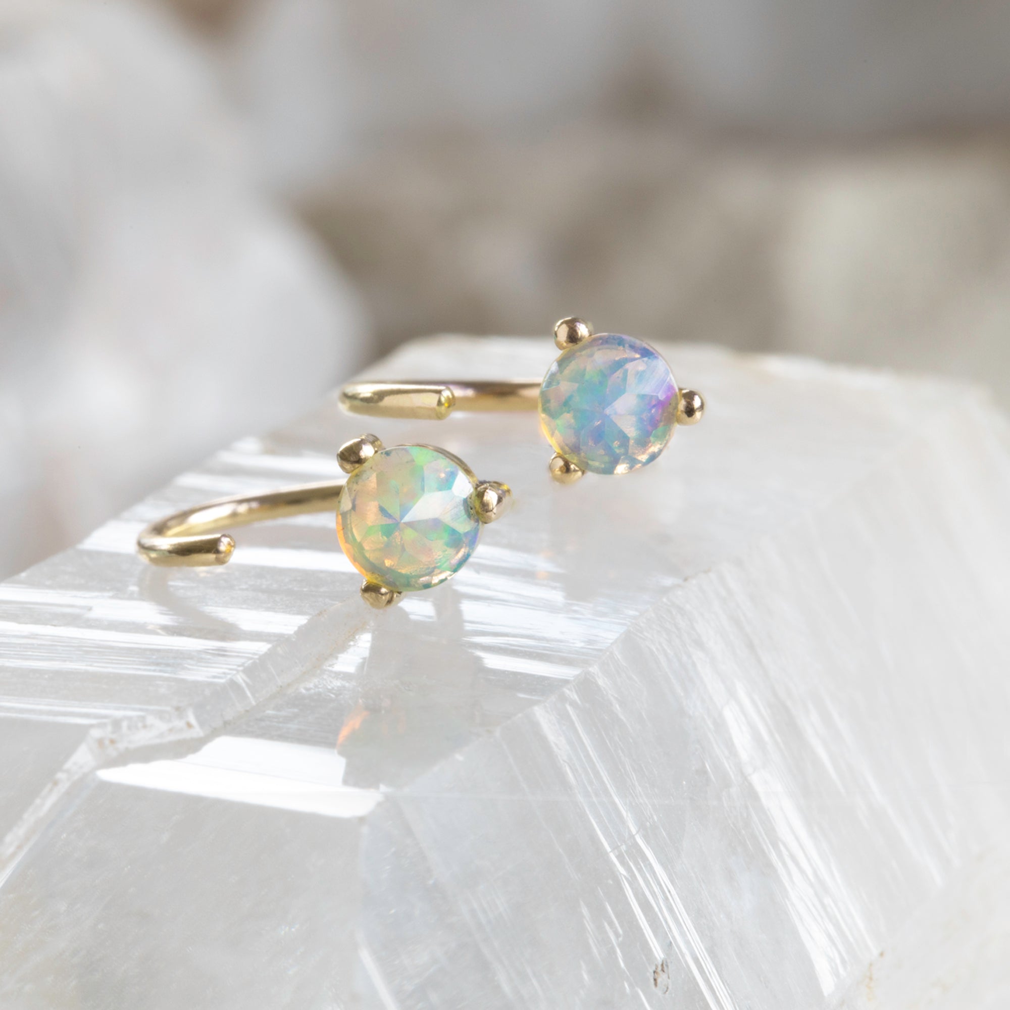 The Opal Huggie Stud Earrings in 14K Yellow Gold laying on white crystal