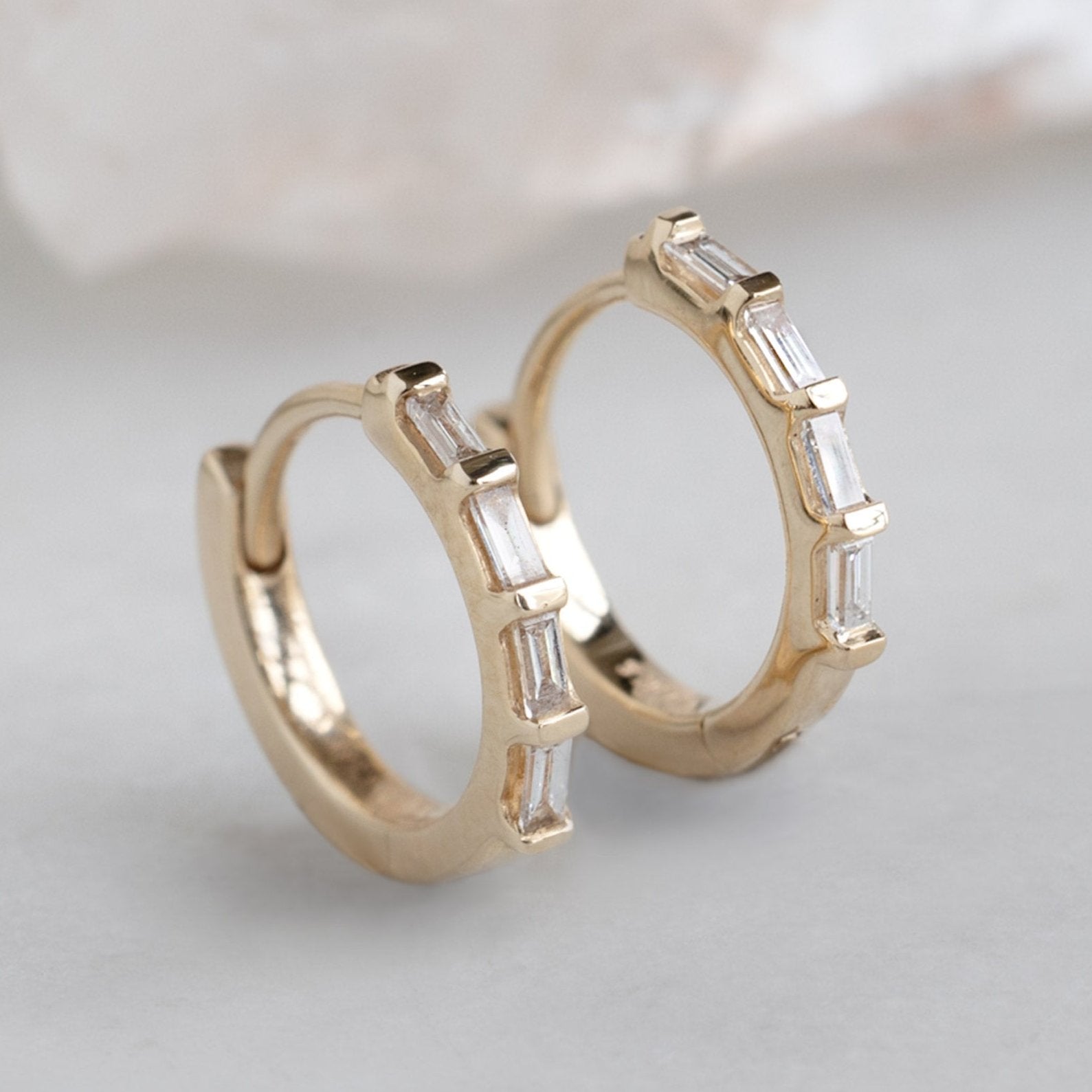 The Baguette White Diamond Huggie Hoops in 14K Yellow Gold on White Marble