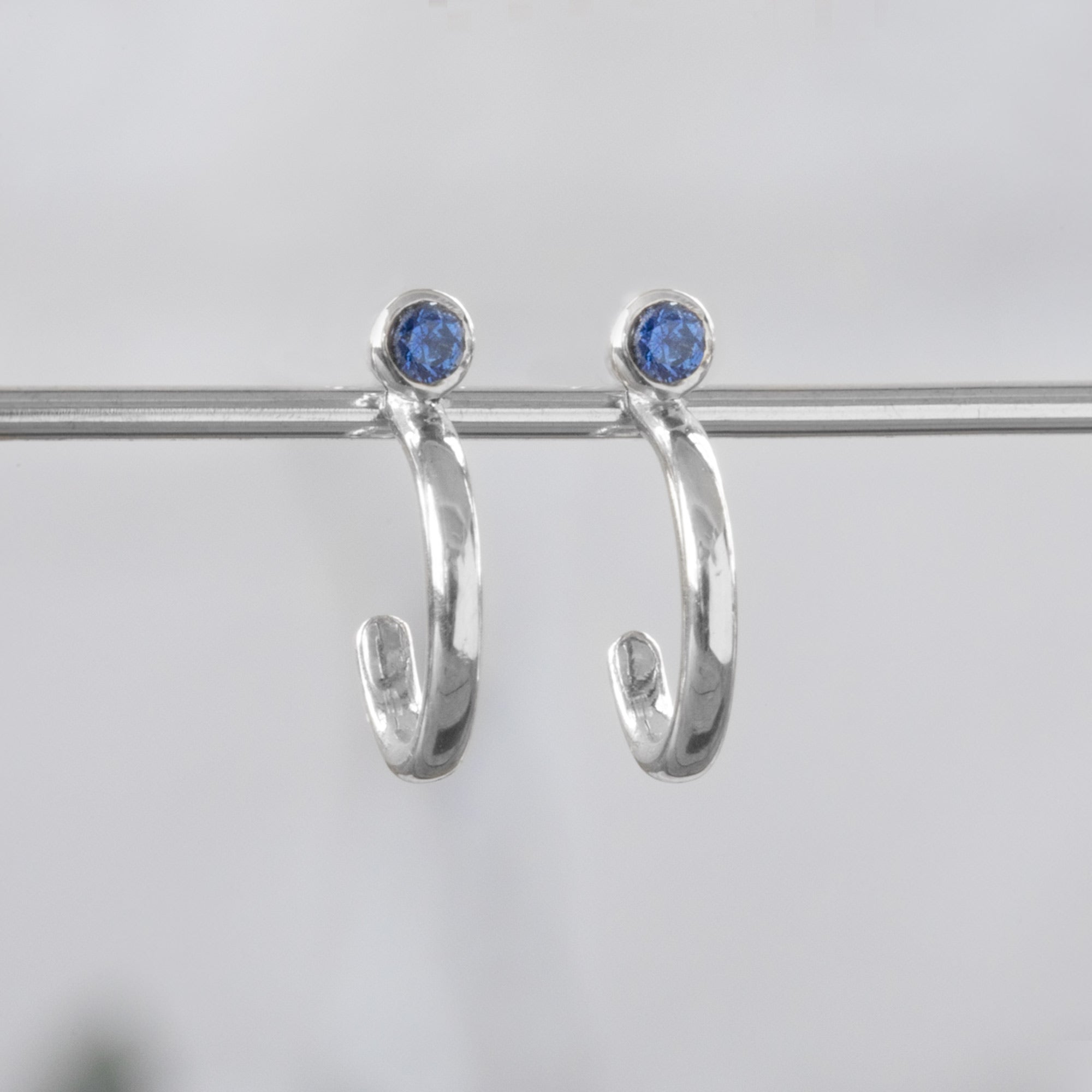 Custom Blue Sapphire Birthstone Hoop Earrings | 14K White Gold displayed on bar with white background.