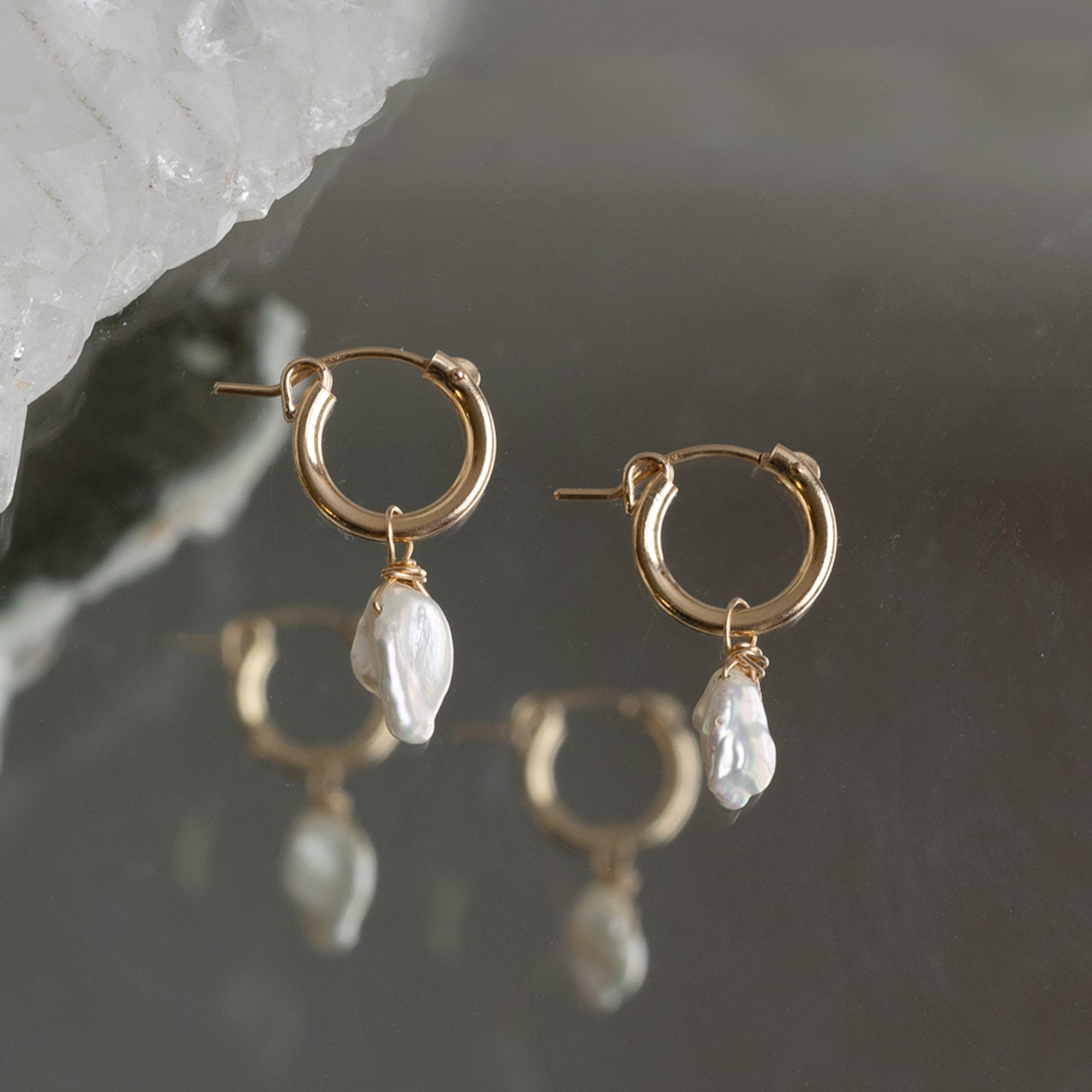 The Keshi Pearl Hoop Earrings in Yellow Gold Filled laying on mirror
