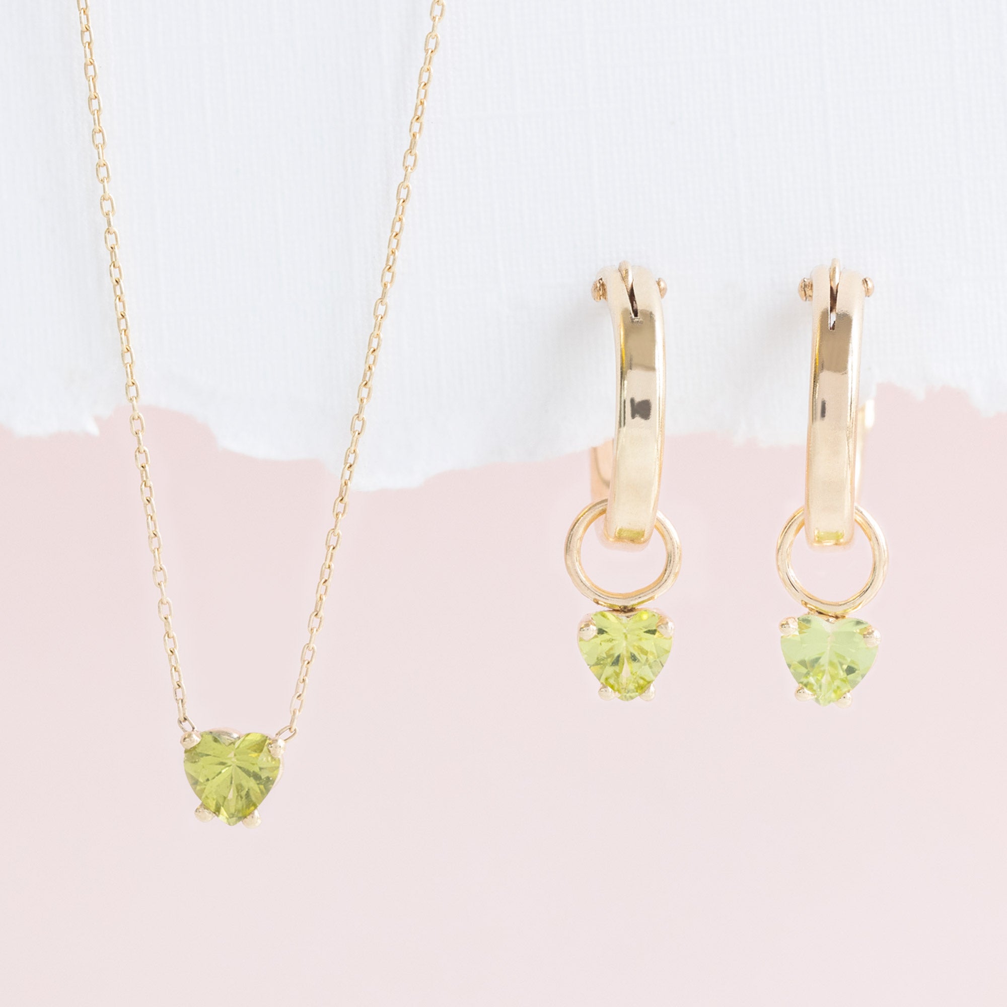 Peridot Heart Fine Jewelry Necklace and Hoop Earrings hanging in front of white textured paper