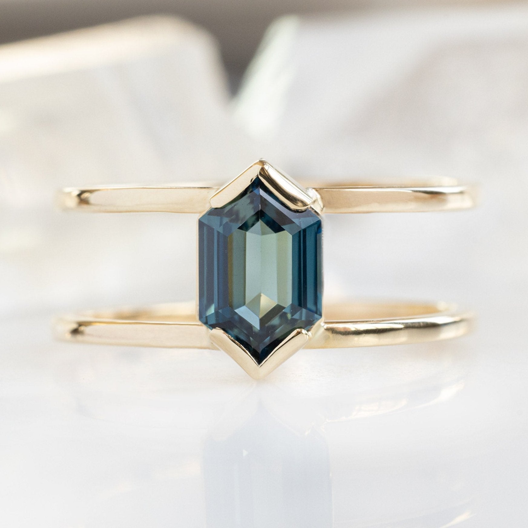 The Poppy Ring with a 1.24ct Hexagon Blue Sapphire in 14K Yellow Gold on White Marble