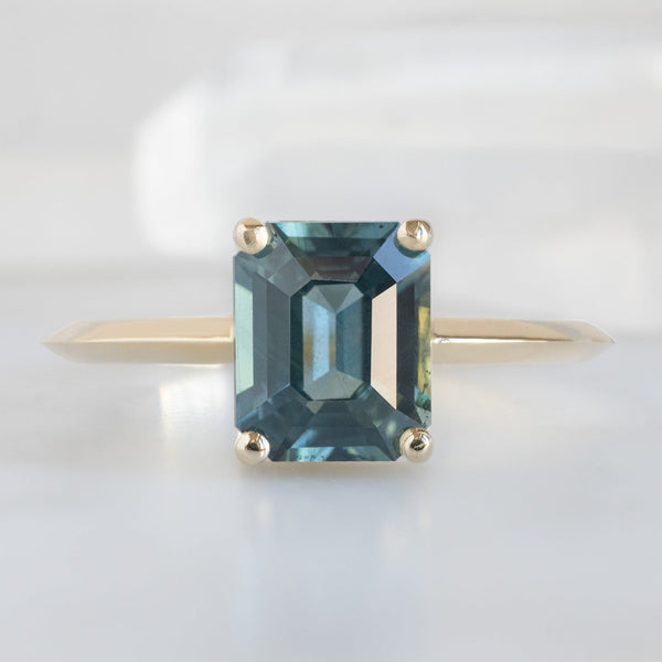 The Bryn Ring with a 1.78ct Emerald Cut Sapphire in 14K Yellow Gold on White Marble