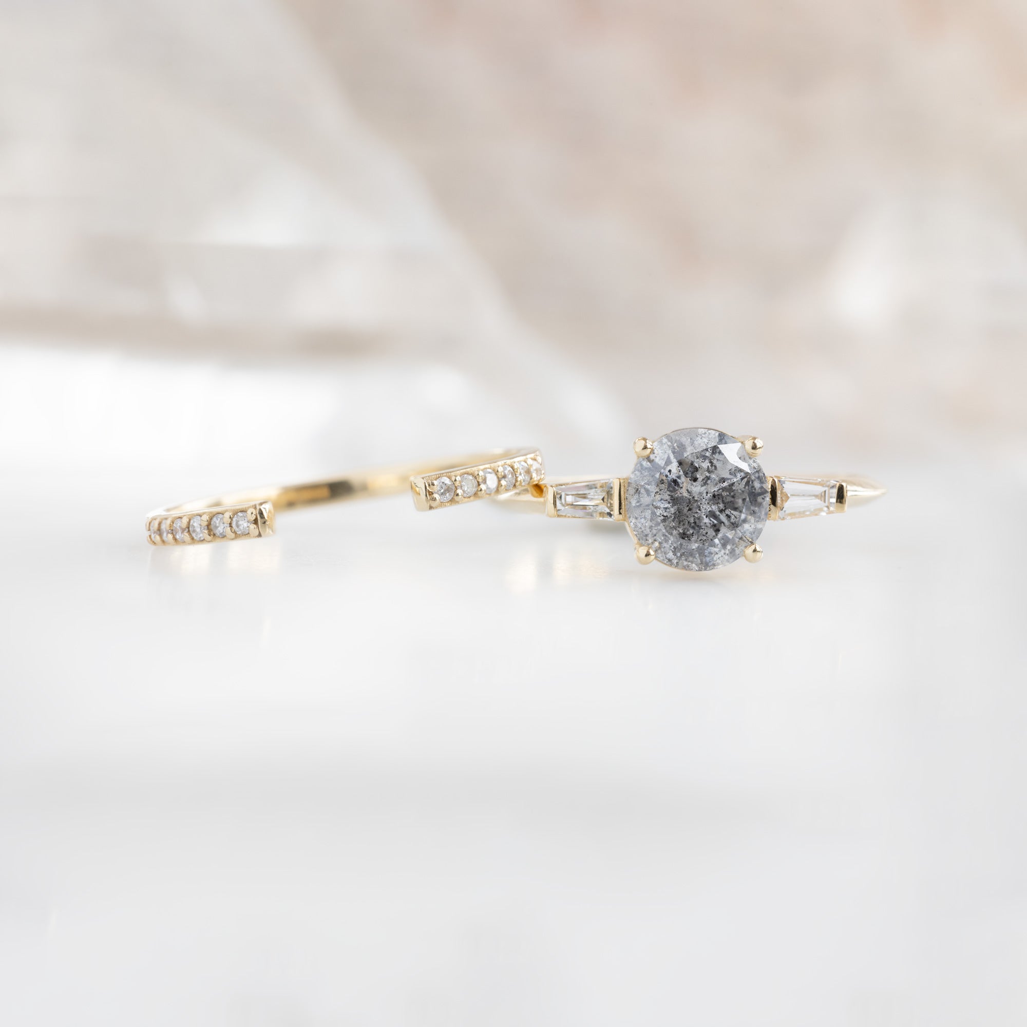 The Ash Ring | 1.22 carat Round Salt and Pepper Diamond in 14K Yellow Gold with white blurred background. displayed next to the open cuff flush pavé wedding band.