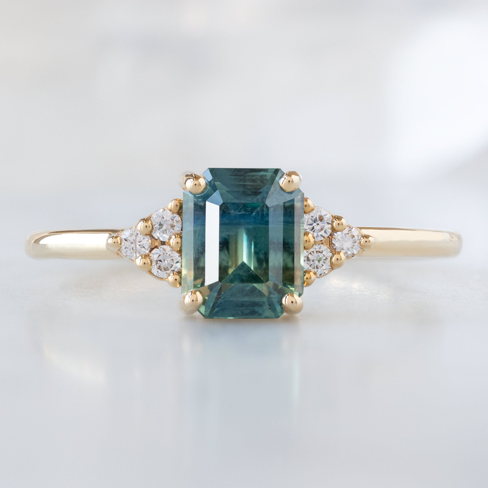 The Ivy Ring with a 1.06ct Emerald Cut Teal Sapphire in 14K Yellow Gold on Marble