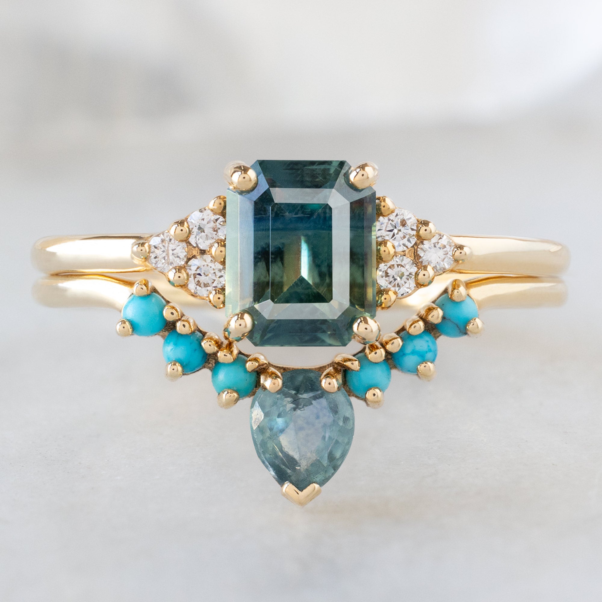 The Ivy Ring with a 1.06ct Emerald Cut Teal Sapphire in 14K Yellow Gold Stacked with the Sapphire ad Turquoise Sunburst Stacking Band