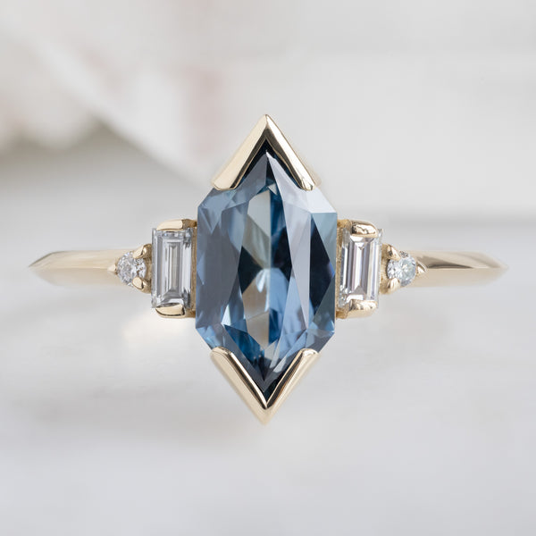 The Primrose Ring with a 1.54ct Blue Sapphire Hexagon in 14K Yellow Gold on White Marble