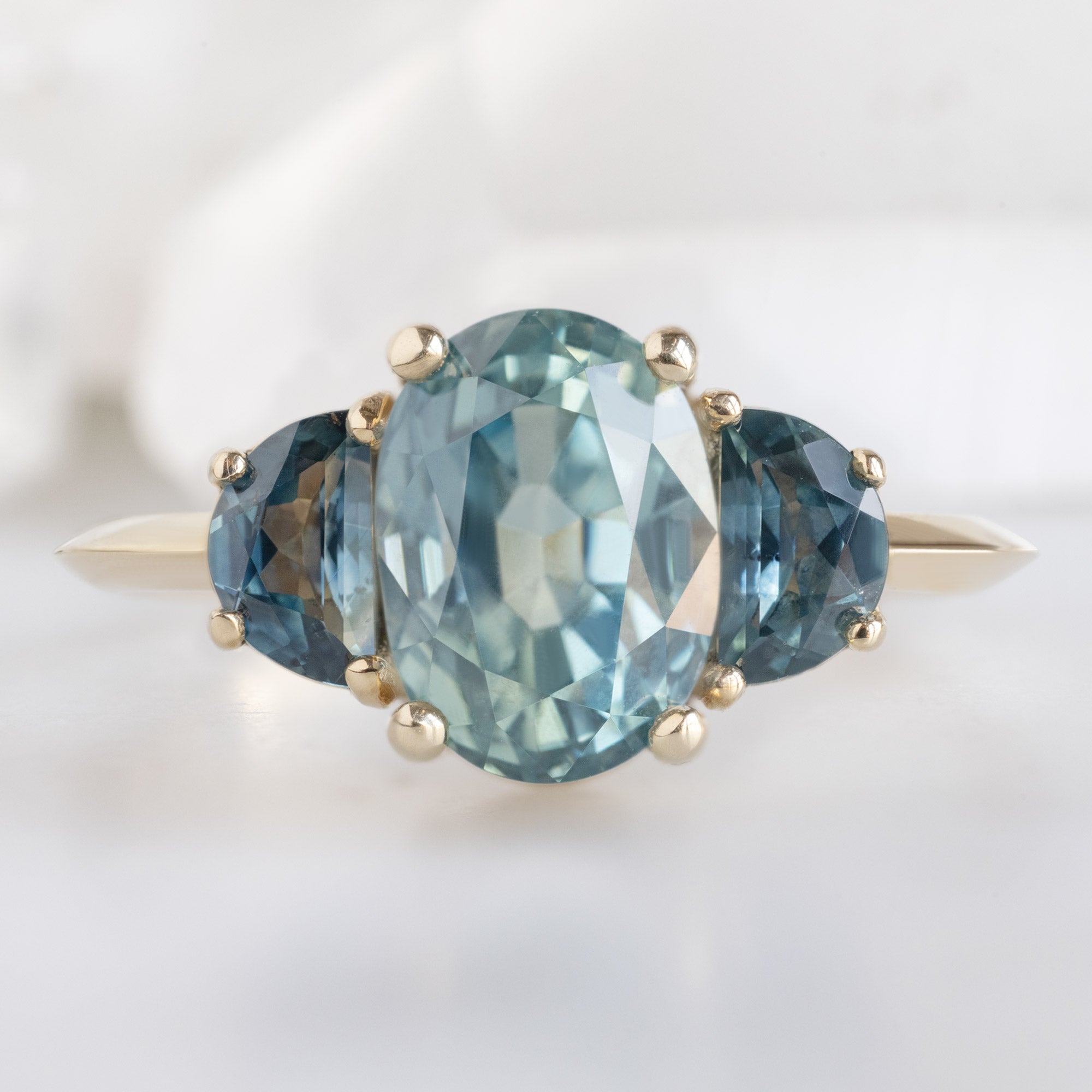 The 3 Stone Ring with a 2.42ct Oval Sapphire in 14K Yellow Gold on White Marble
