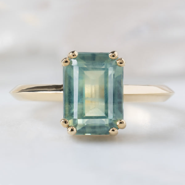 The Bryn Ring with a 2.97ct Emerald Cut Bi-Color Sapphire in 14K Yellow Gold on White Marble Tile
