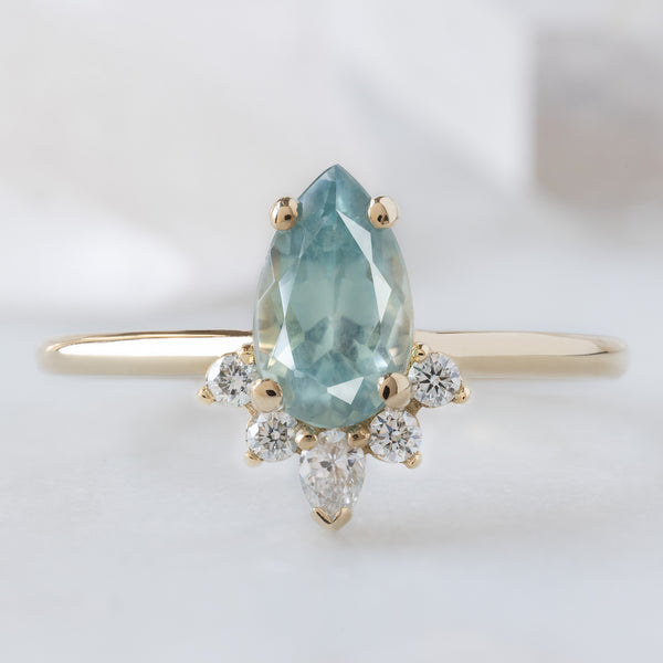 The Aster Ring with a 1.18ct Pear Blue Sapphire in 14K Yellow Gold on White Marble