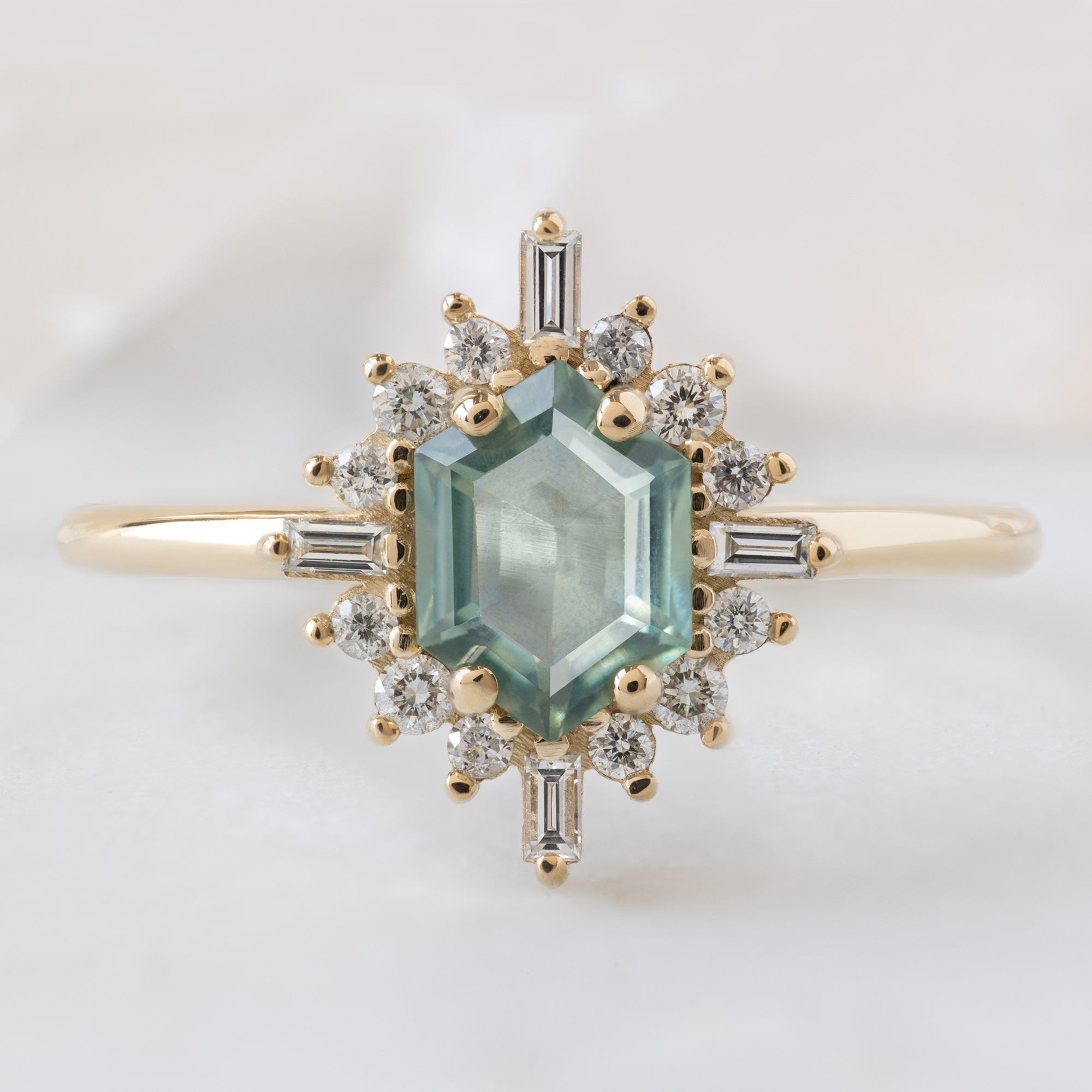 The Compass Ring with a 0.77ct Hexagon Montana Sapphire in 14K Yellow Gold on White Marble Tile