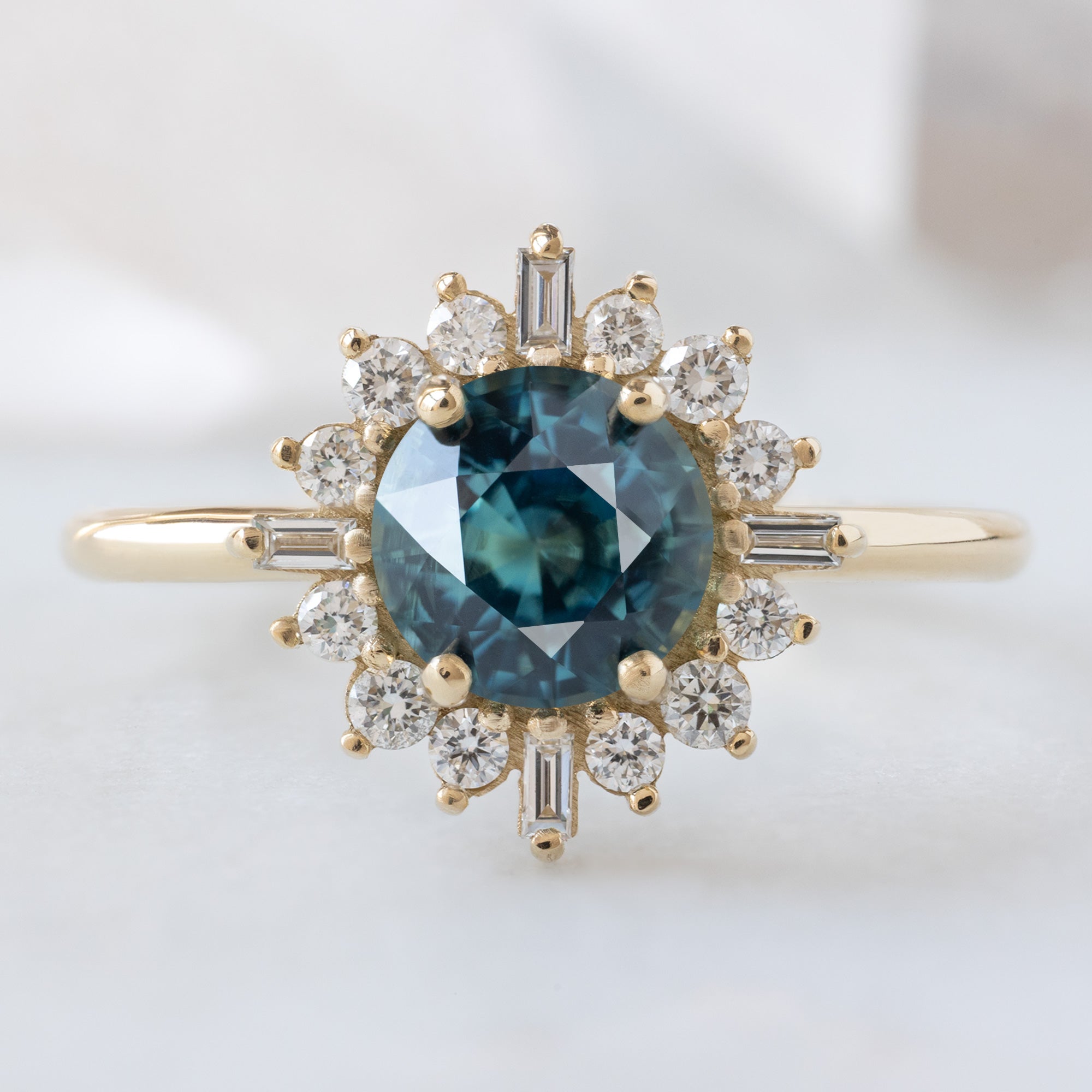 The Compass Ring with a 1.19ct Round Blue Sapphire in 14K Yellow Gold on White Marble