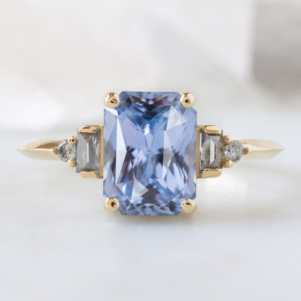 The Primrose Ring with a 2.36ct Emerald Cut Sapphire in 14K Yellow Gold on White Marble Surface