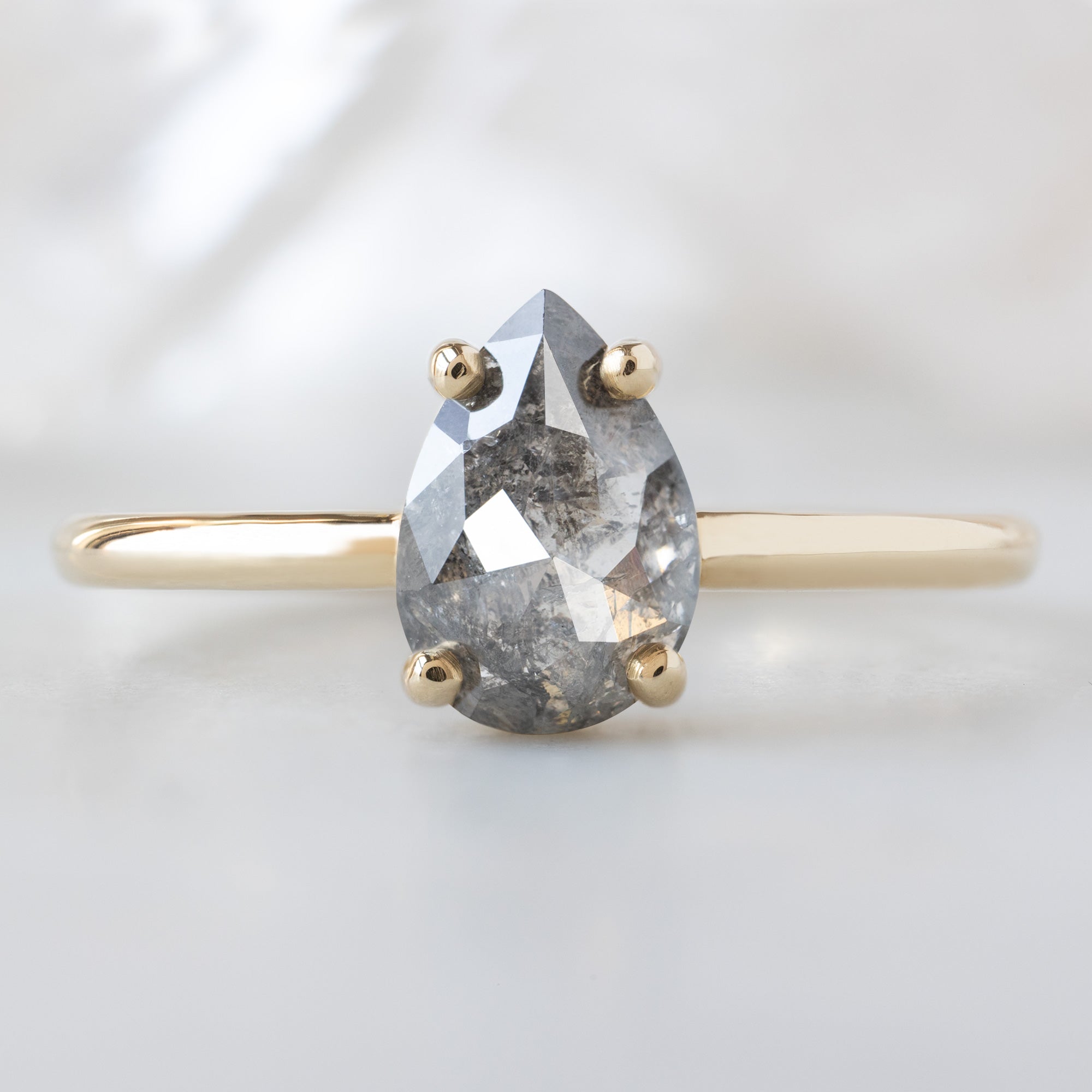 The Bryn Ring with a 1.01ct Pear Salt and Pepper Diamond in 14K Yellow Gold on White Marble Surface