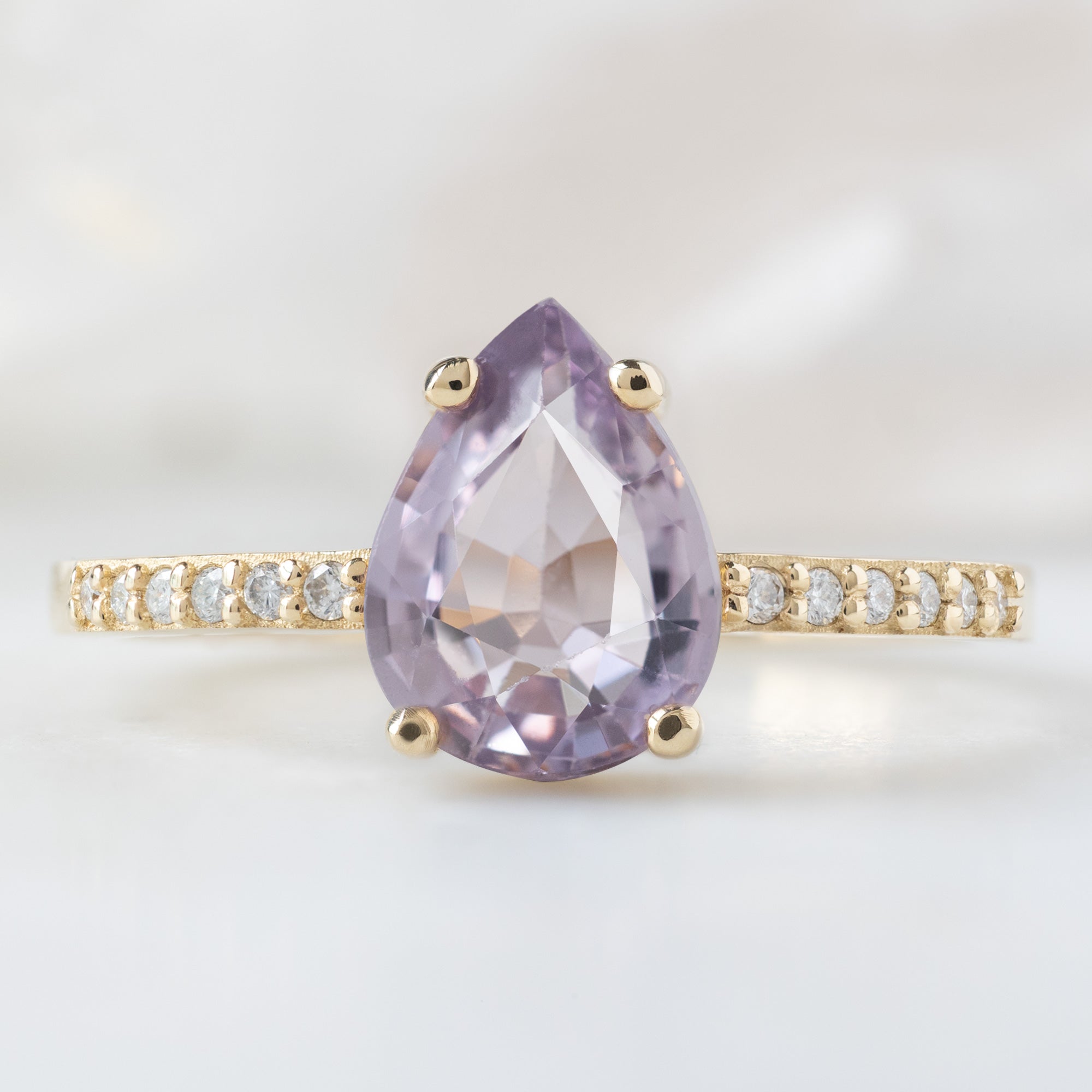 The Willow Ring with a 1.38ct Pear Violet Sapphire in 14K Yellow Gold on White Marble