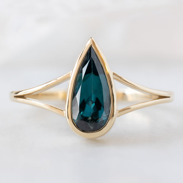 The Magnolia Ring with a 1.48ct Pear Blue Sapphire in 14K Yellow Gold on White Marble Surface