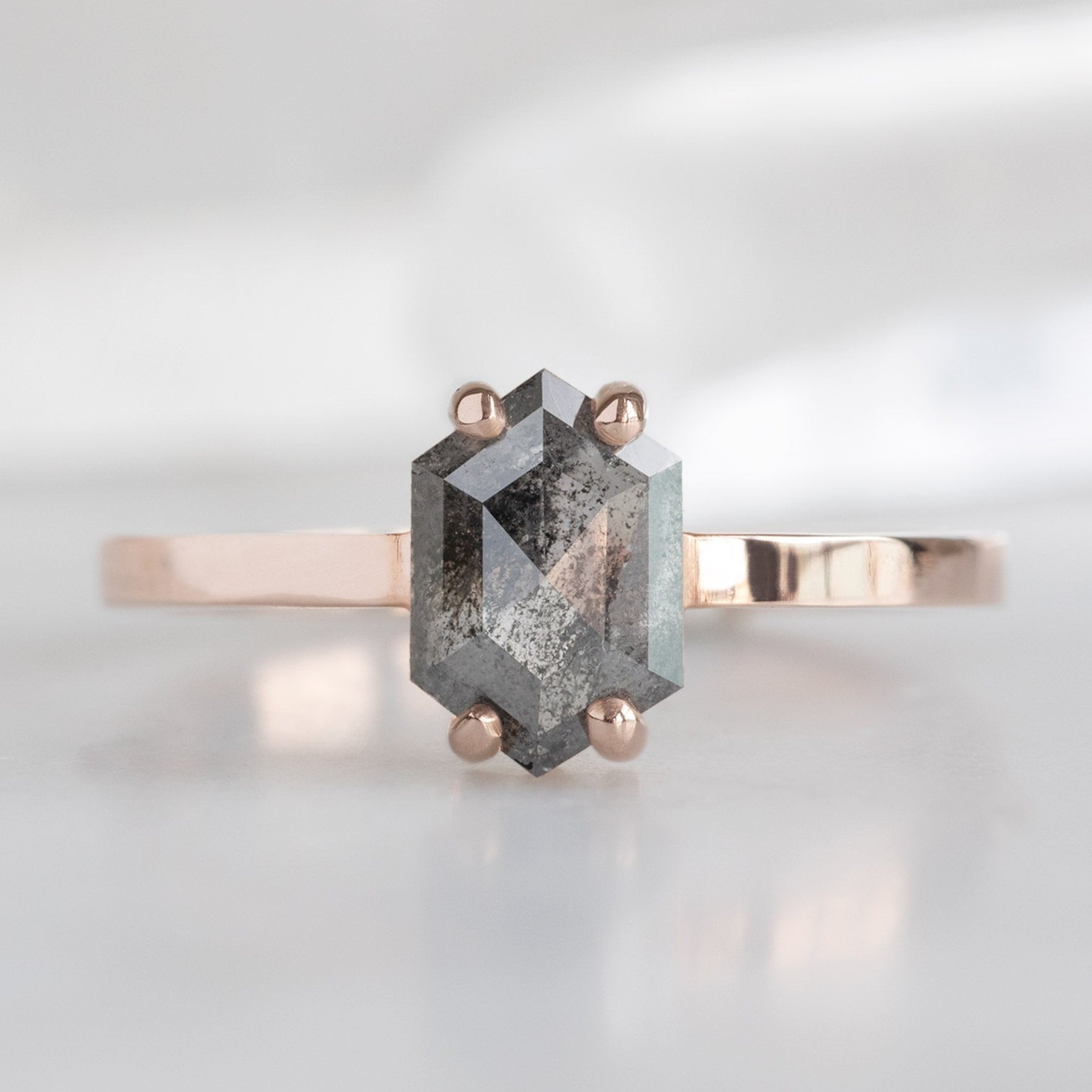 The Bryn Ring with a 0.88 carat Black Hexagon Diamond in 14K Rose Gold displayed on a marble surface.
