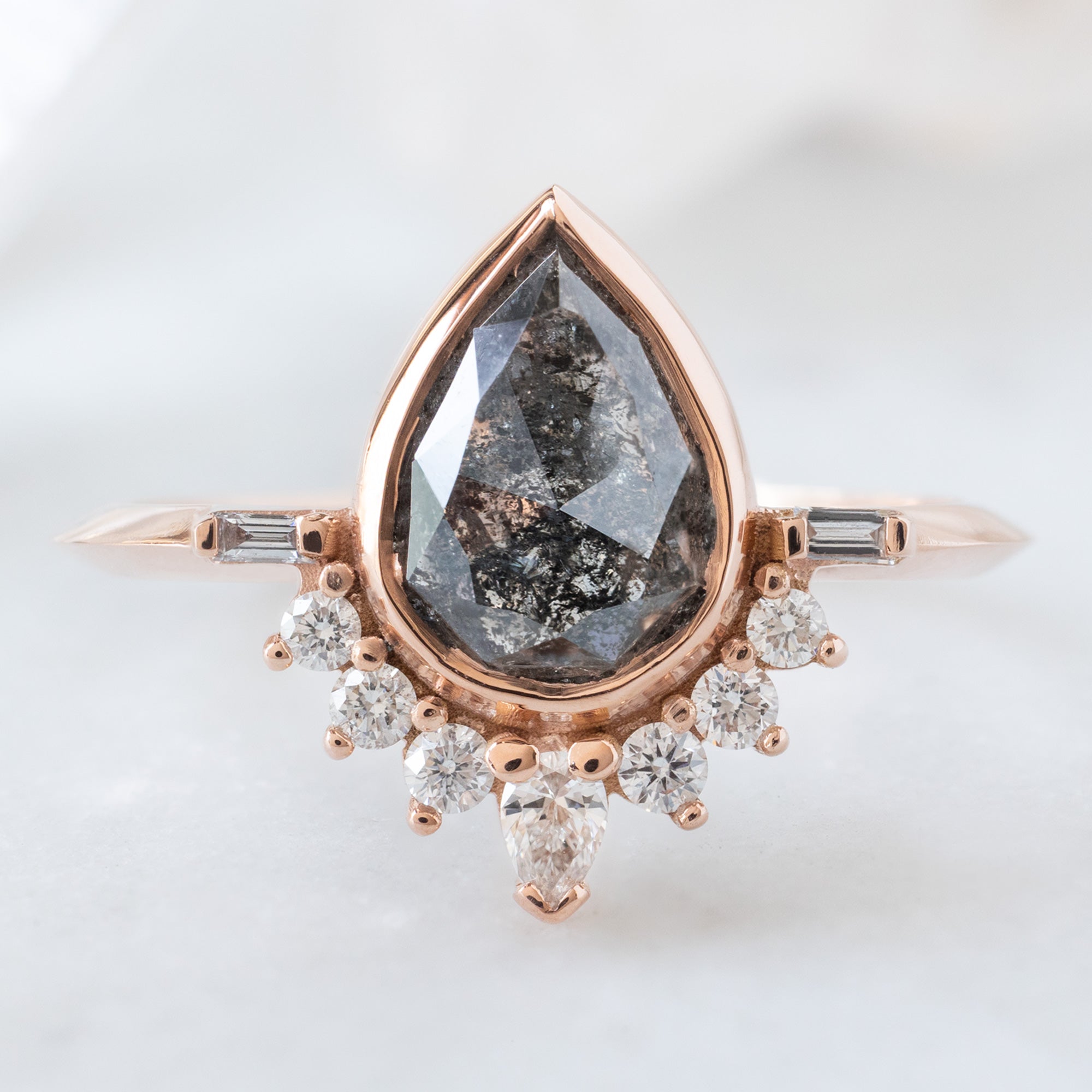The Posy Ring with a 1.32ct Pear Black Diamond in 14K Rose Gold on White Marble Surface