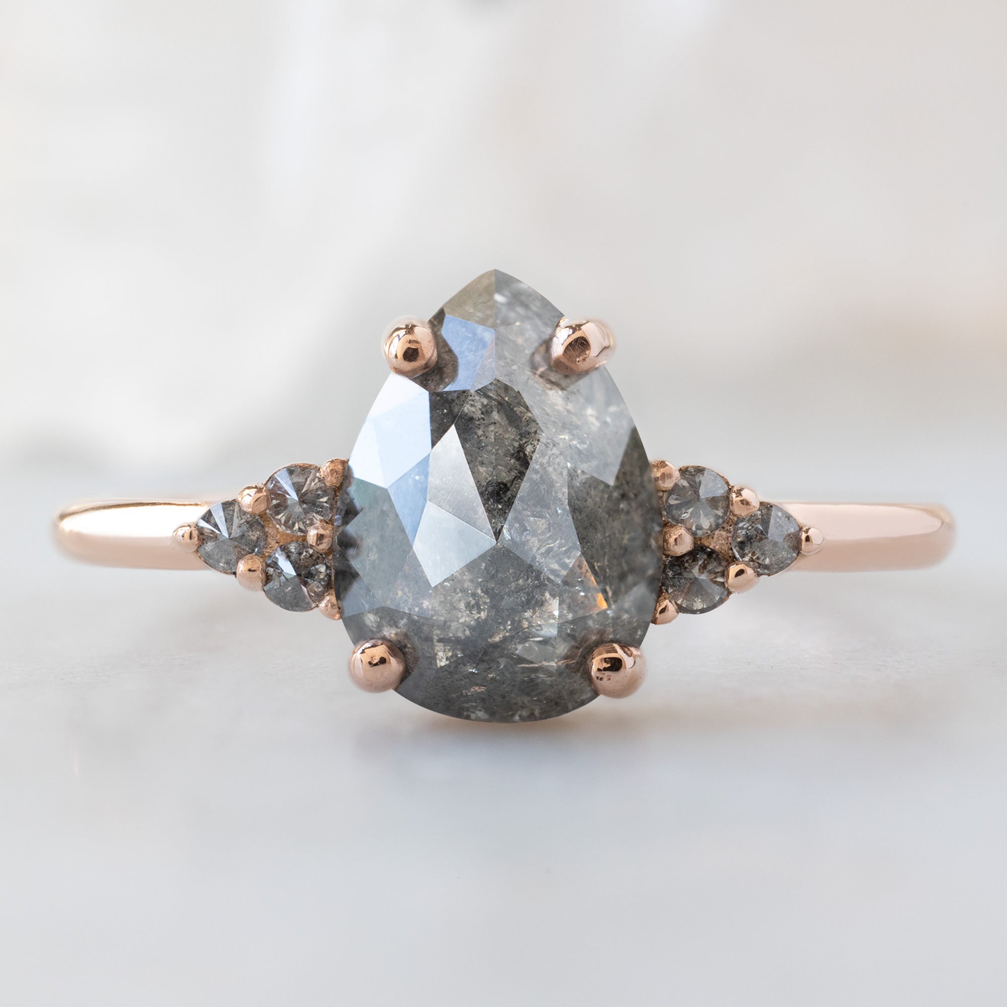 The Ivy Ring with a 1.43ct Pear Salt and Pepper Diamond in 14K Rose Gold on White Marble Surface