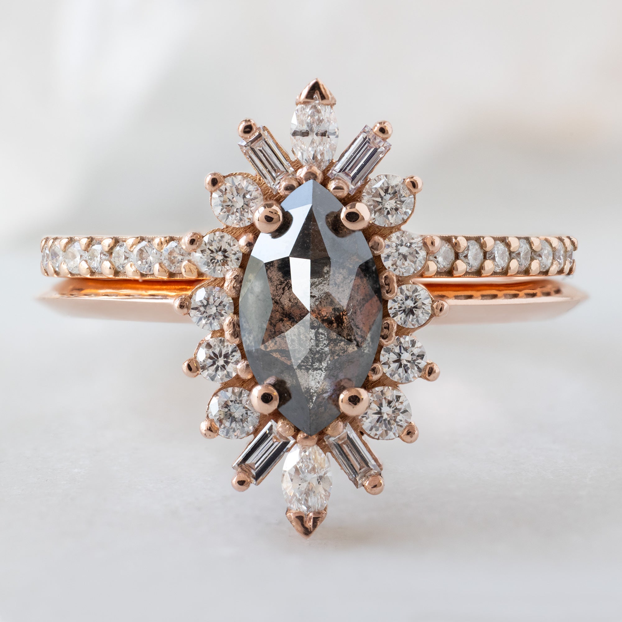 The Camellia Ring with a .66ct Marquise Salt and Pepper Diamond in 14K Rose Gold Stacked with the White Diamond Pavé Stacking Band on White Marble Surface