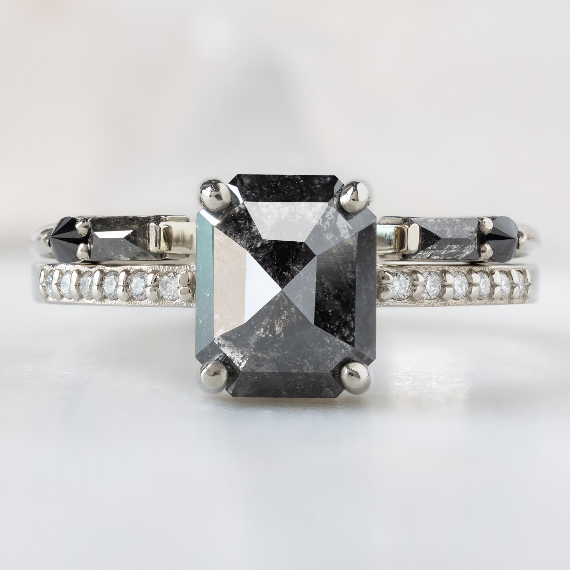 The Willow Ring with a 1.53ct Emerald Cut Black Diamond in 14K White Gold Stacked with the Luxe Open Cuff Black Diamond Stacking Band on White Marble Surface