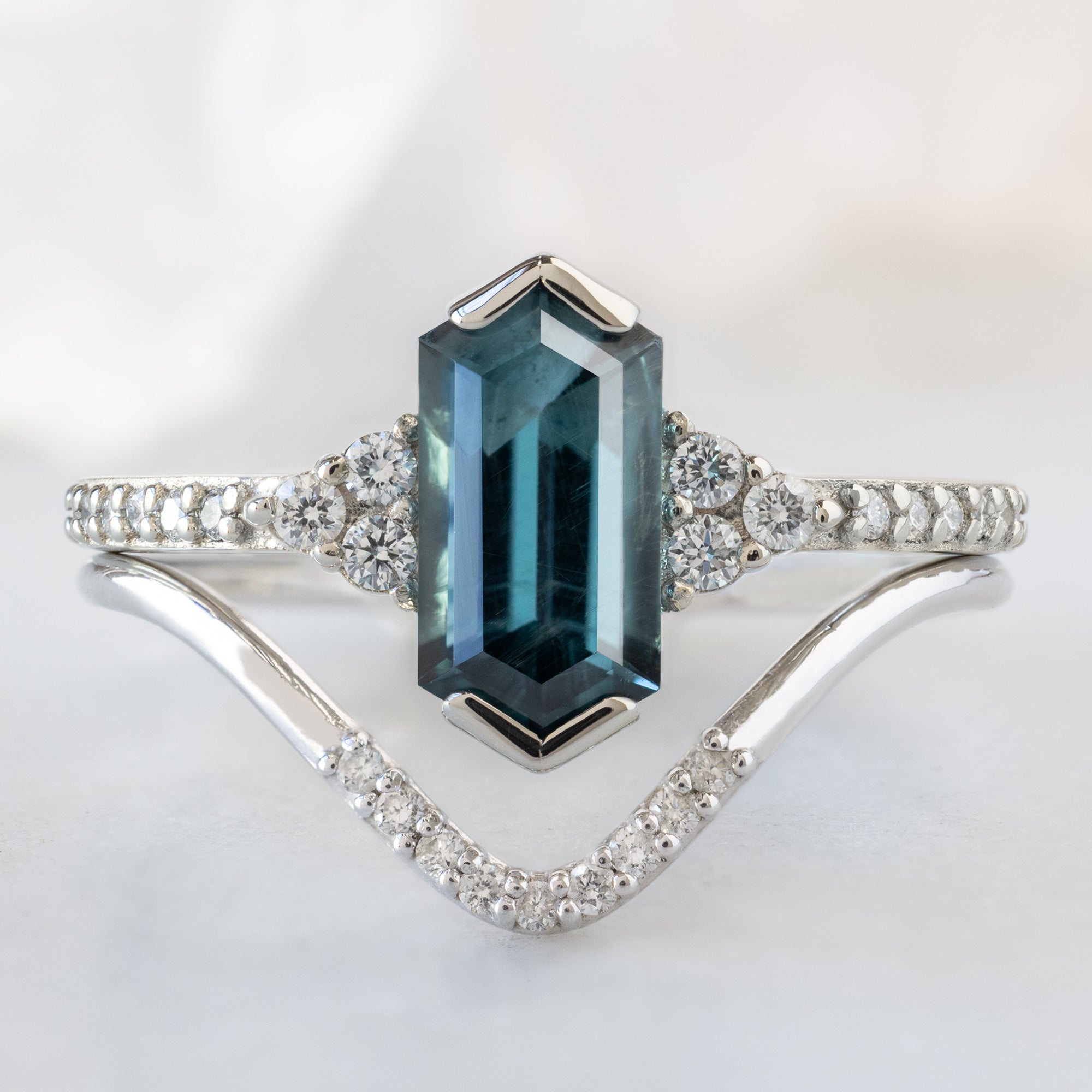 The Ivy Ring with a 1.22ct Hexagon Blue Spinel in 14K White Gold Stacked with the White Diamond Pavé Peak Stacking Band on White Marble Surface
