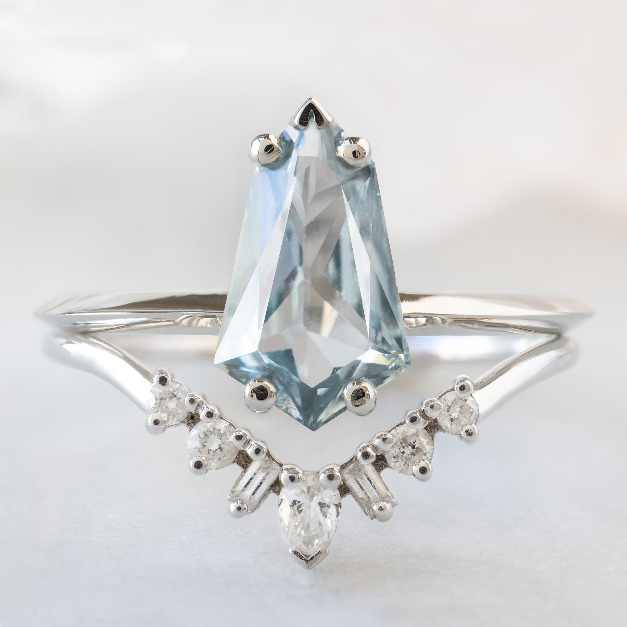 The Sage Ring with a 1.44ct Geometric Blue Sapphire in 14K White Gold Stacked with the Geometric Diamond Sunburst Stacking Band on White Marble Surface