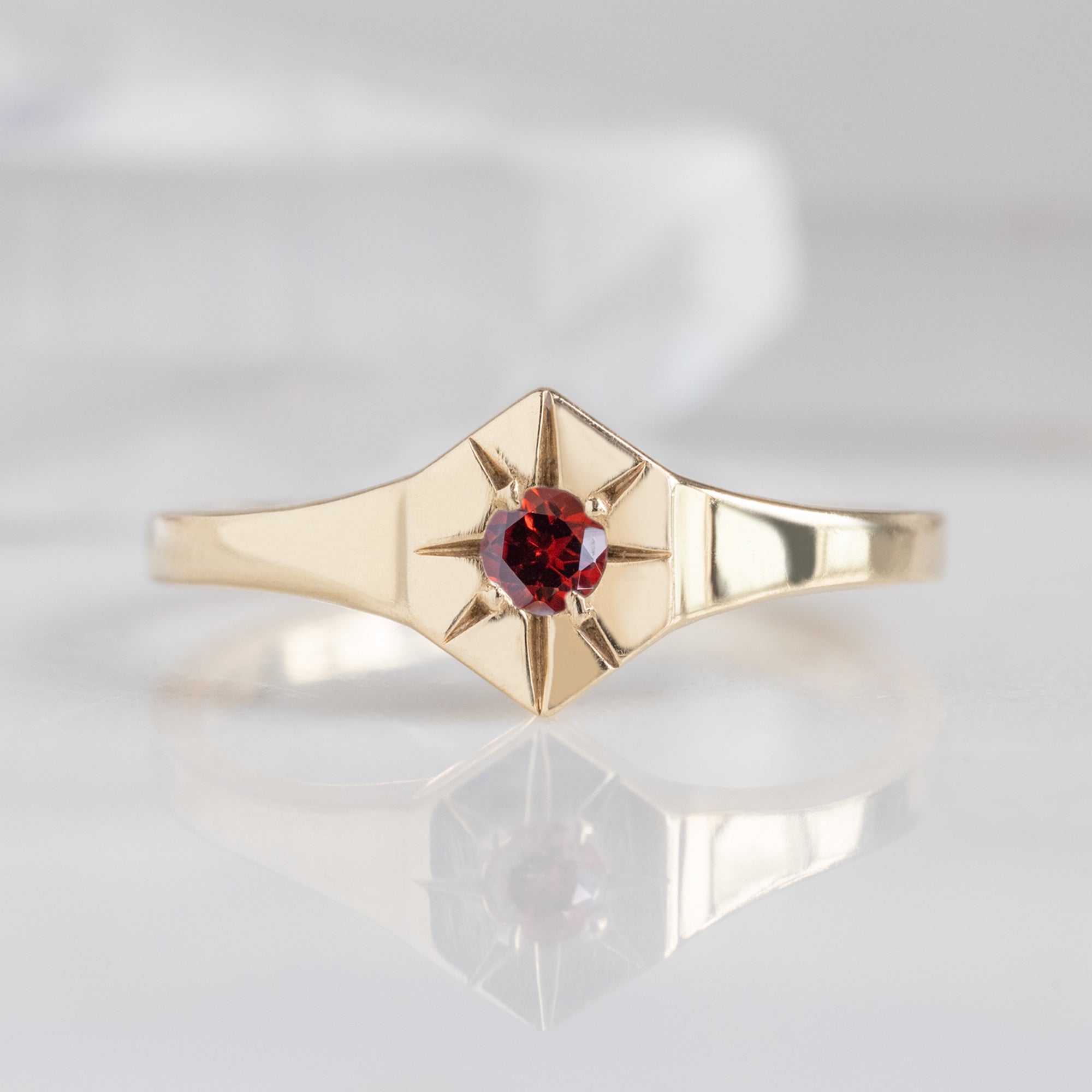 Custom Garnet Birthstone Signet Ring | 10K Yellow Gold. Displayed on marble surface with white blurred background.