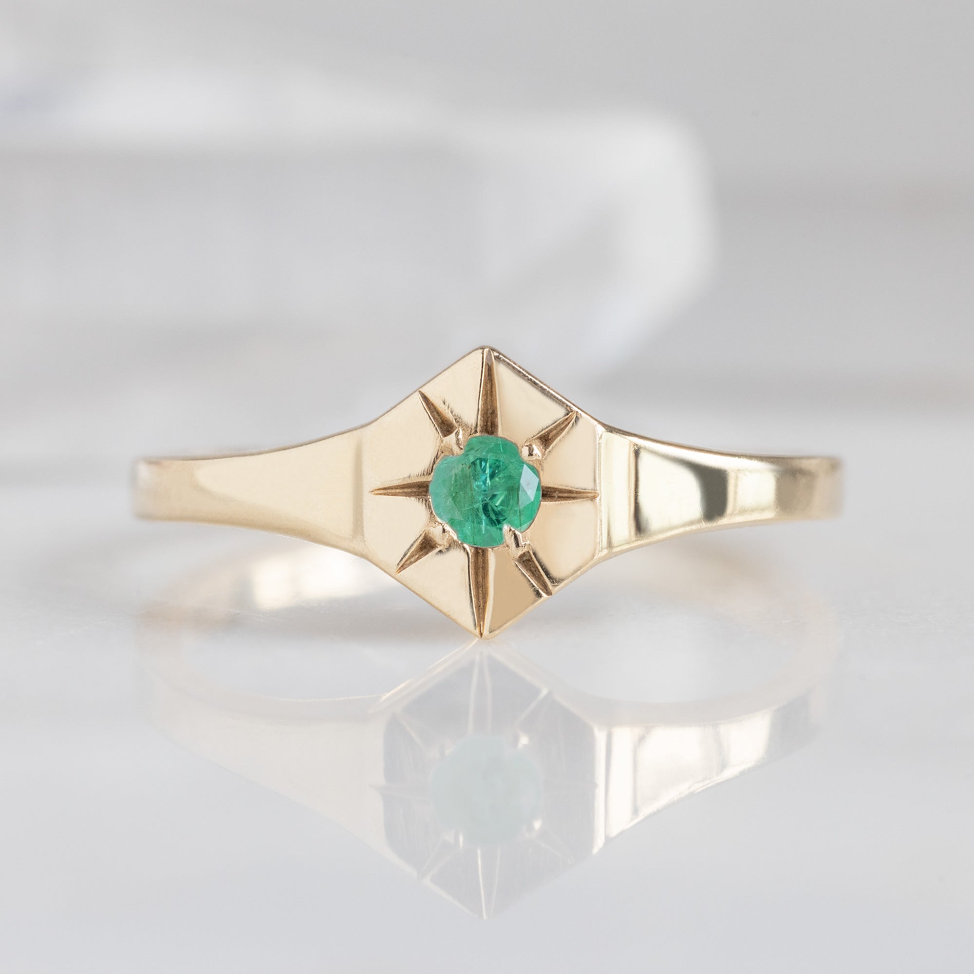 Custom Emerald Birthstone Signet Ring | 10K Yellow Gold. Displayed on marble surface with white blurred background.