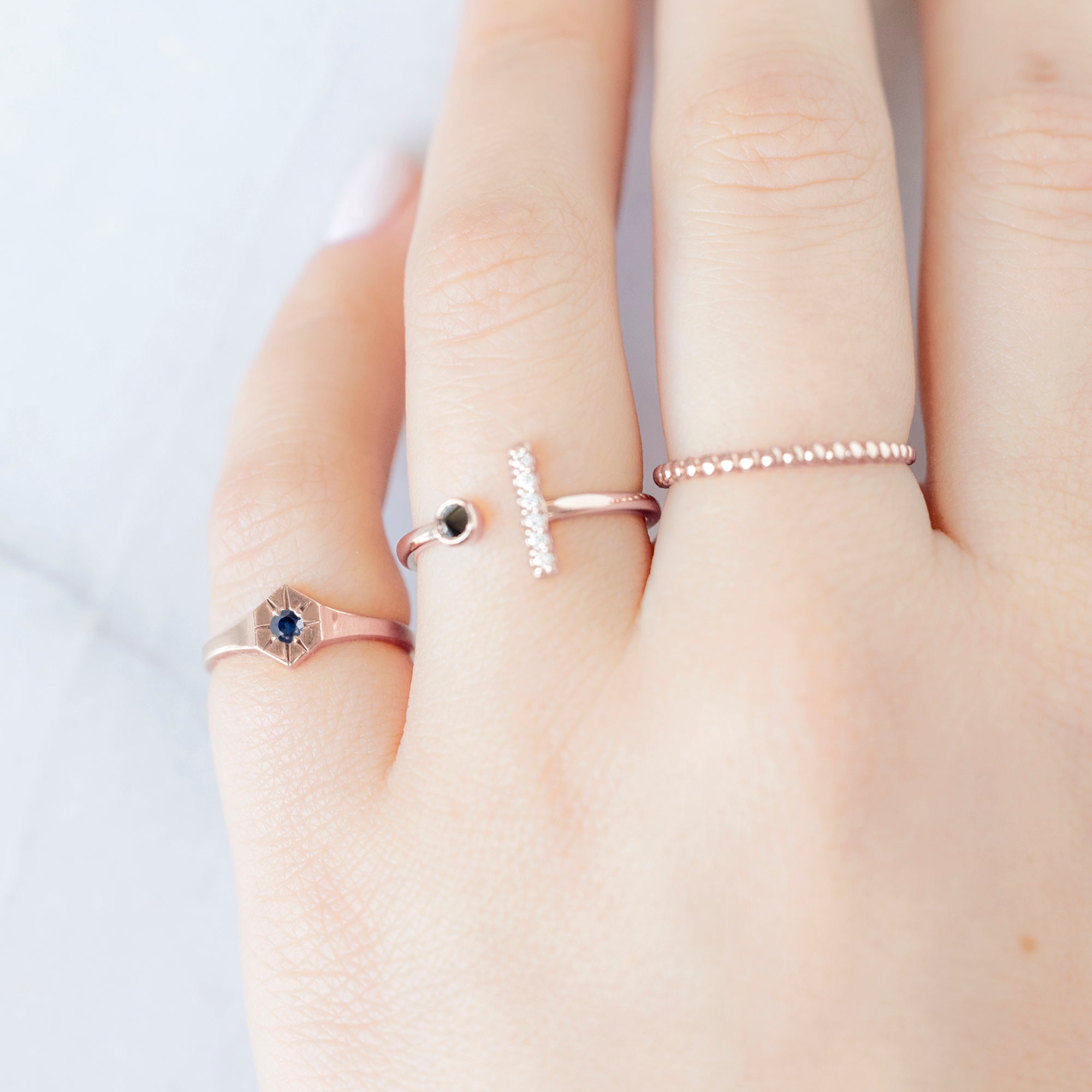 Custom Blue Sapphire Birthstone Signet Ring | 10K Rose Gold. Displayed on model's lefthand pinky finger alongside two other rings on consecutive fingers.