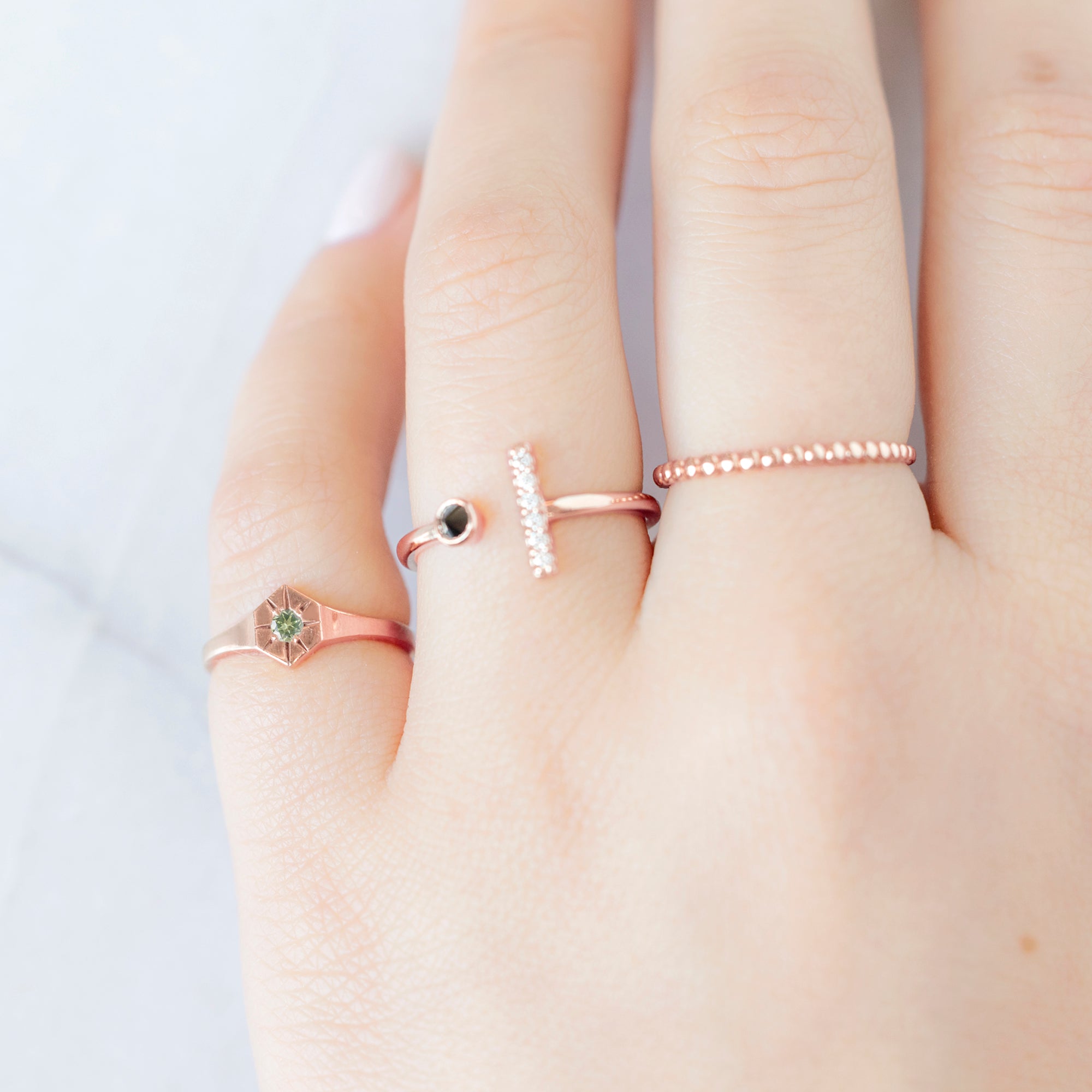 Custom Peridot Birthstone Signet Ring | 10K Rose Gold. Displayed on model's ring finger alongside two other rings on consecutive fingers.