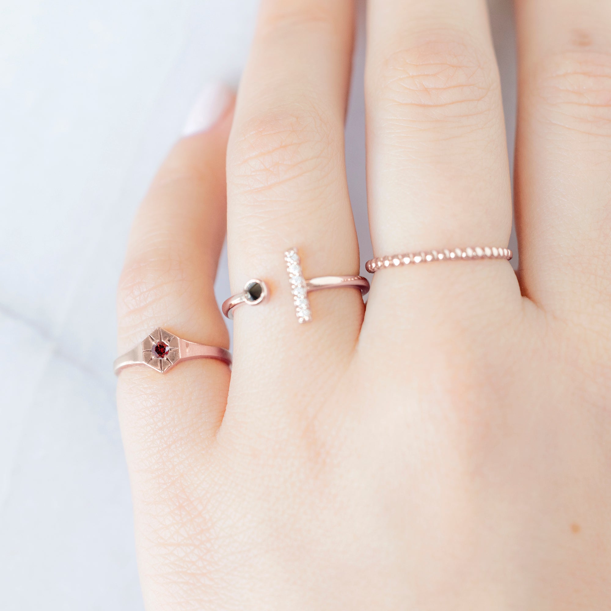 Custom Garnet Birthstone Signet Ring | 10K Rose Gold. Displayed on model's left hand pinky finger alongside two other rings on consecutive fingers.
