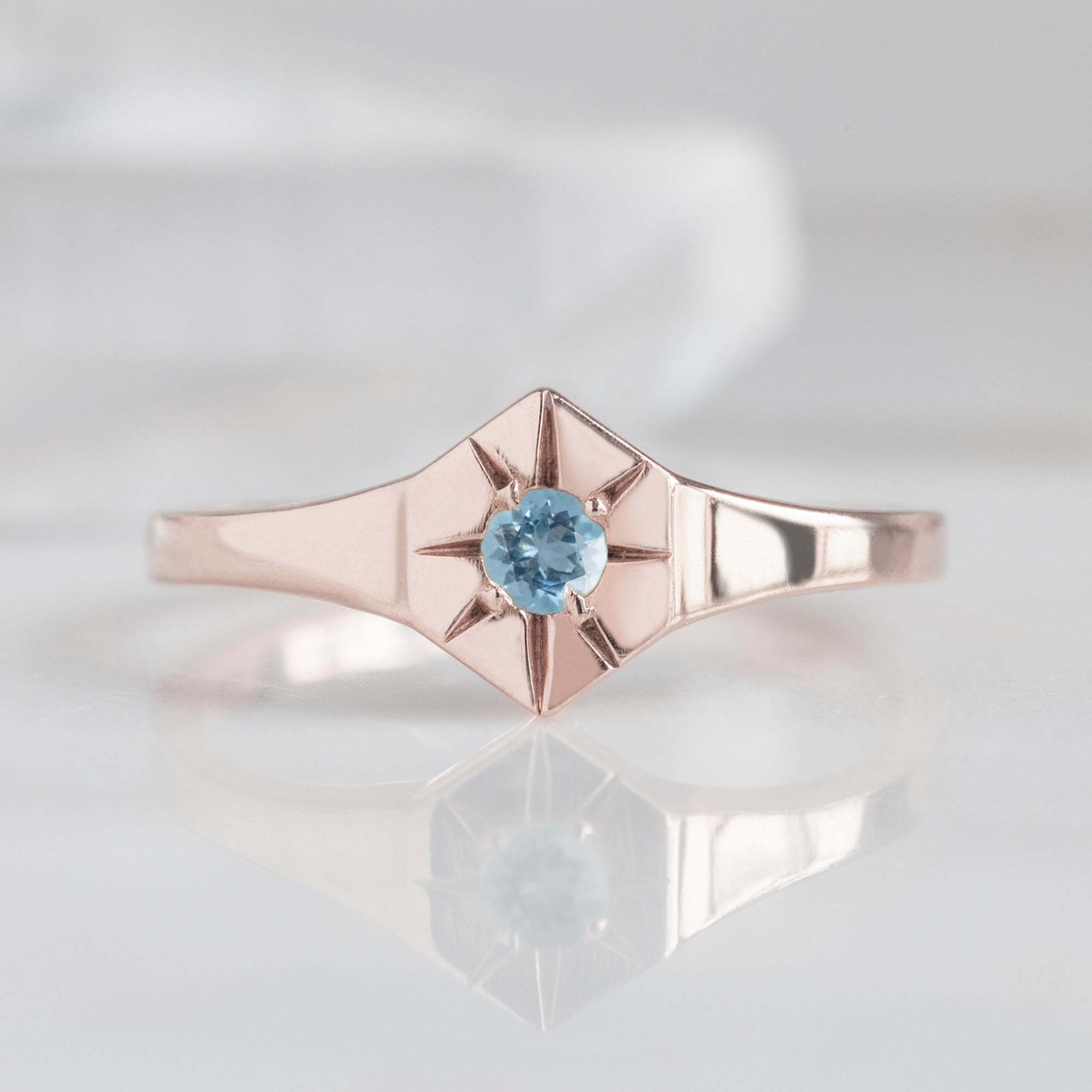 Custom Aquamarine Birthstone Signet Ring | 10K Rose Gold displayed on marble surface with white blurred background.