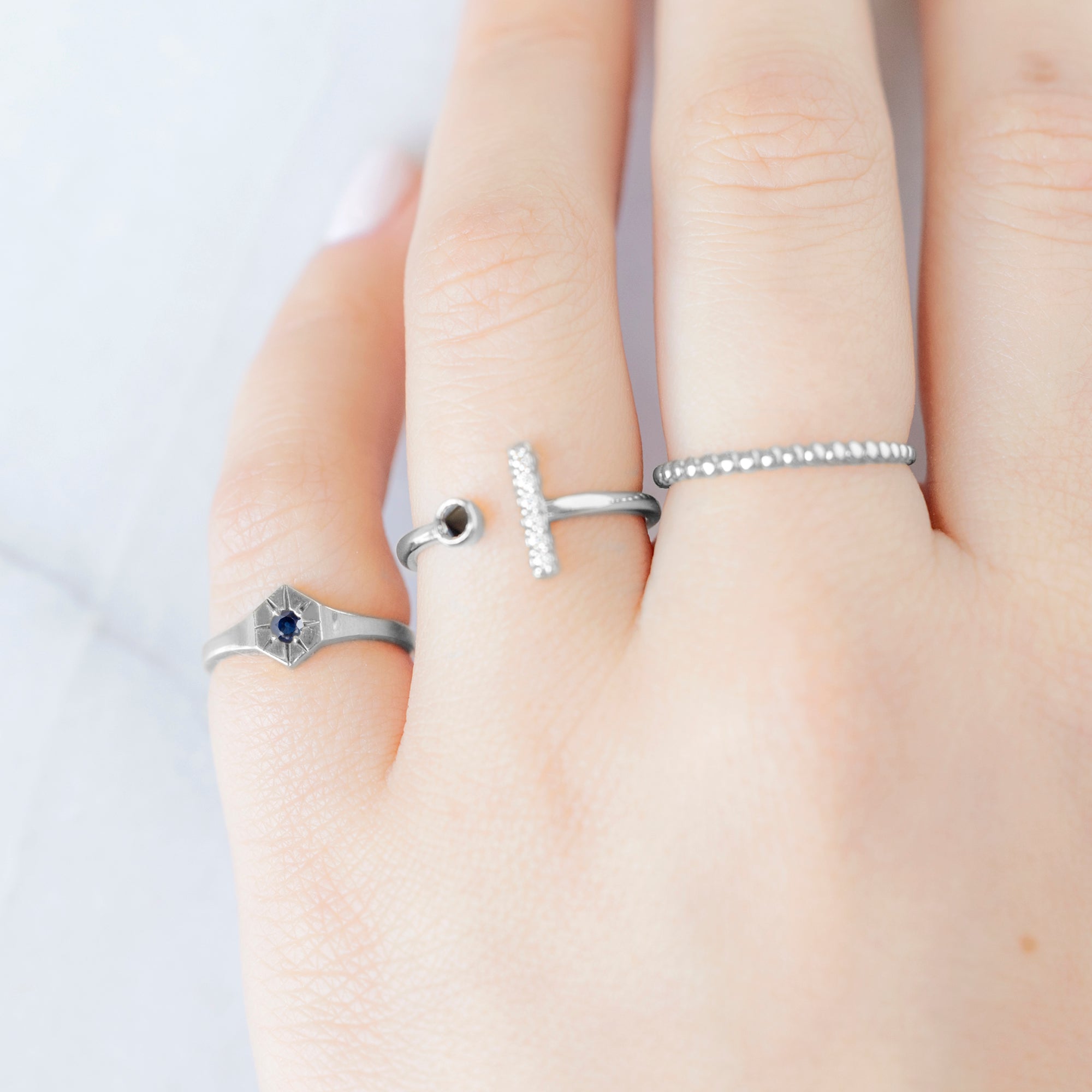 Custom Blue Sapphire Birthstone Signet Ring | 10K White Gold displayed on model's left hand pinky finger alongside two other rings on consecutive fingers.