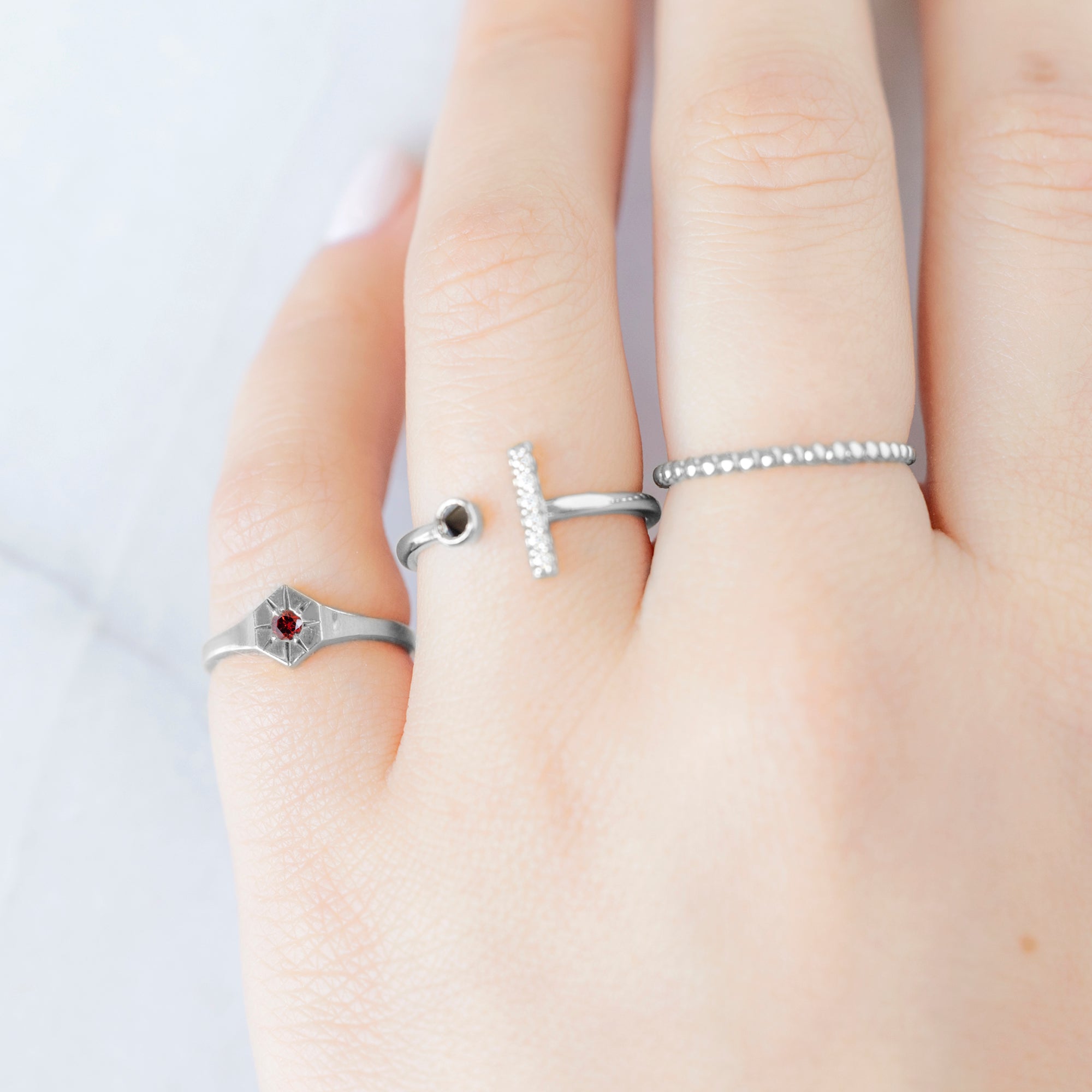Custom Garnet Birthstone Signet Ring | 10K White Gold. Displayed on model's left hand pinky finger, alongside two other rings on consecutive fingers.
