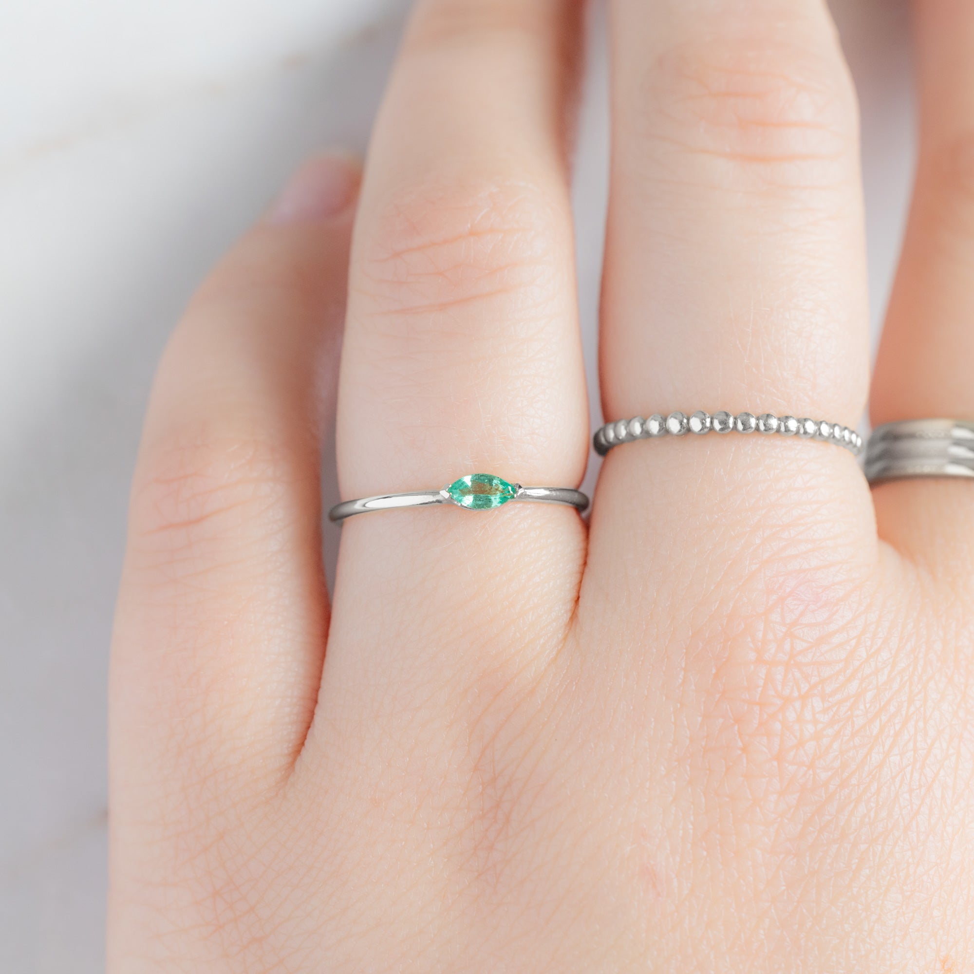 The Teensy Emerald Ring in 14k White Gold stacked on model