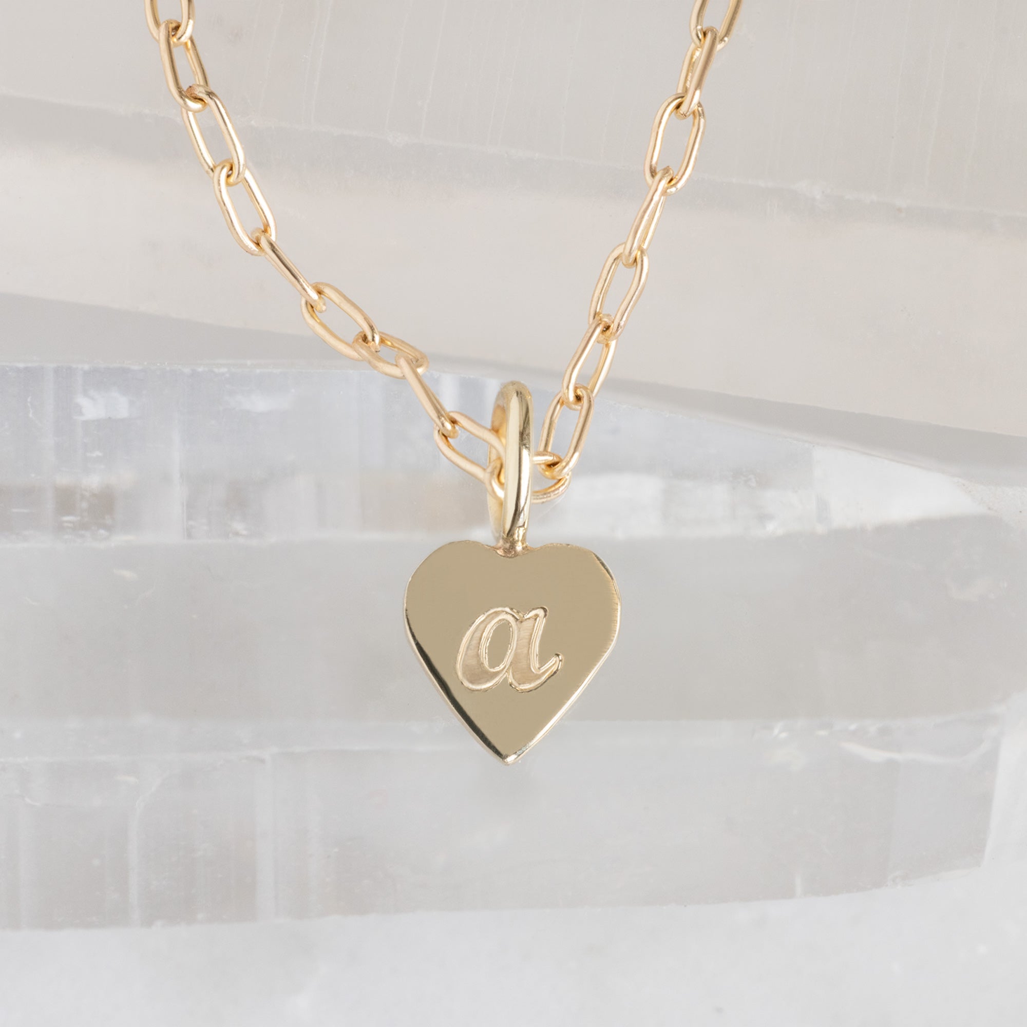 Close up of The Heart Pendant Necklace with an engraved 'A' in Yellow Gold on white crystal surface