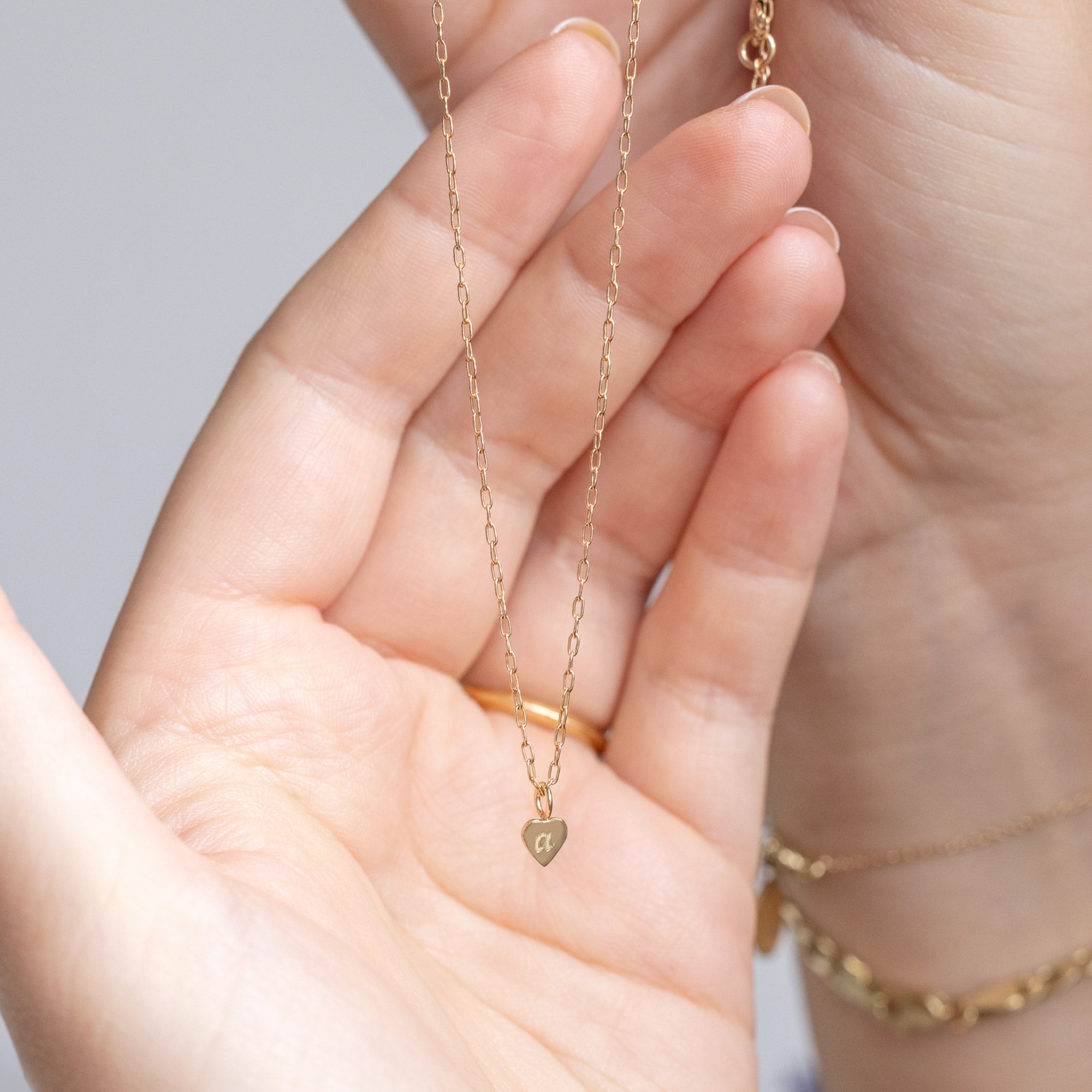 The Heart Pendant Necklace in Yellow Gold with an engraved 'A' held in model's hand