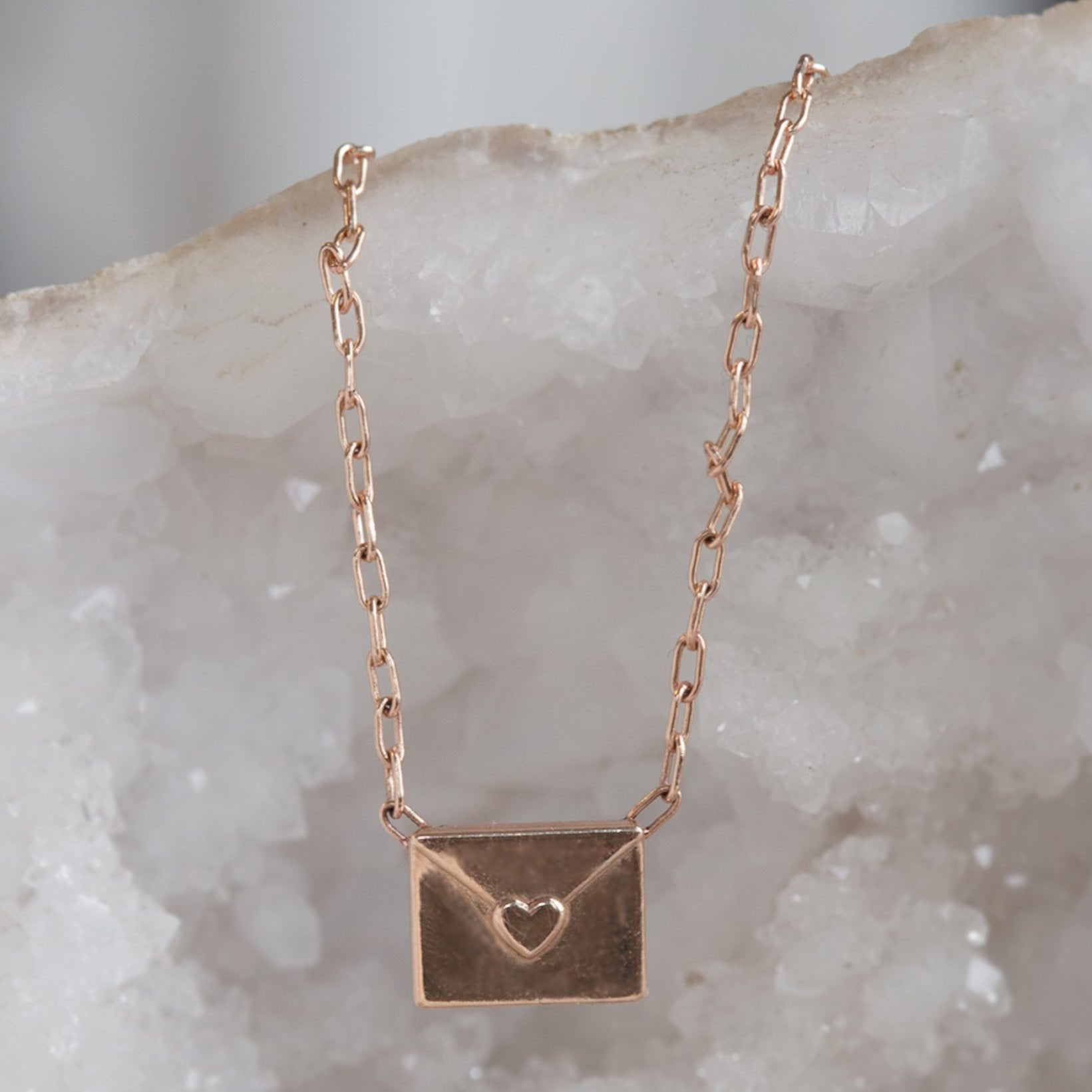 rose gold necklace featuring a loveletter shaped pendant hanging on white geode