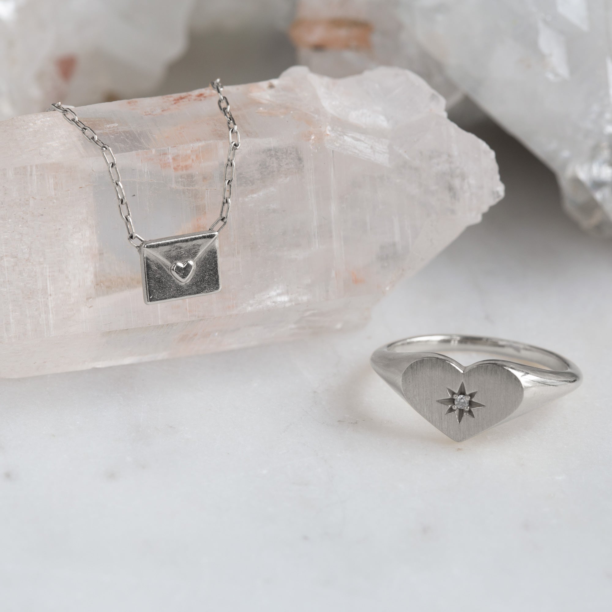 sterling silver necklace featuring a loveletter shaped pendant hanging on white crystal next to heart shaped signet ring