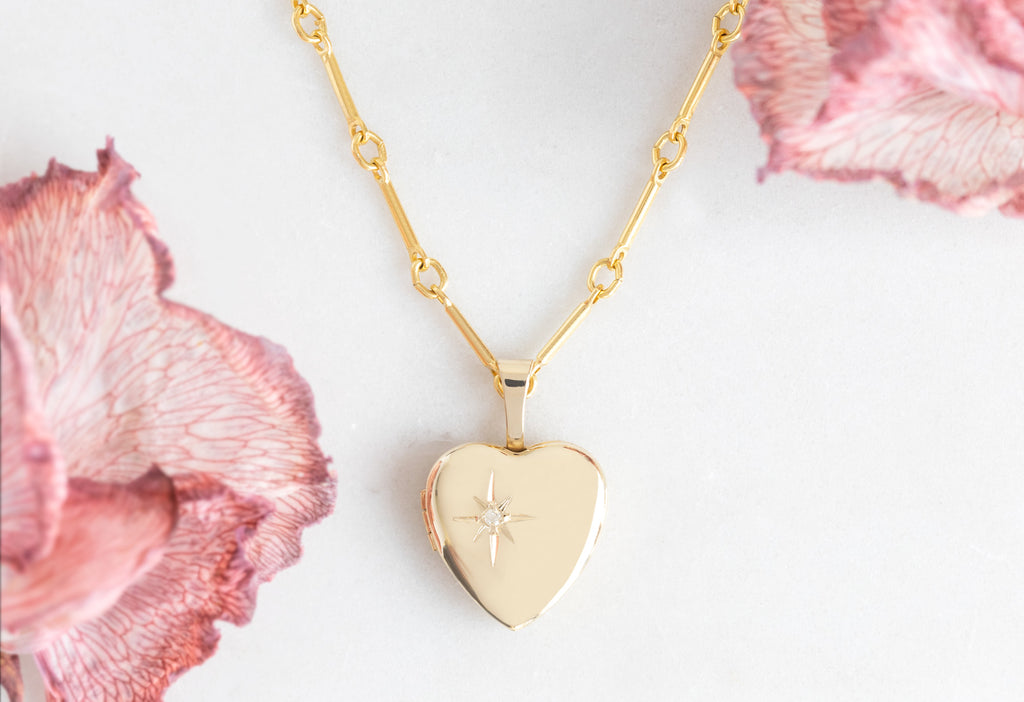 Close Up of Yellow Gold Sweetheart Diamond Locket Necklace on White Marble Tile surrounded by pink flower petals