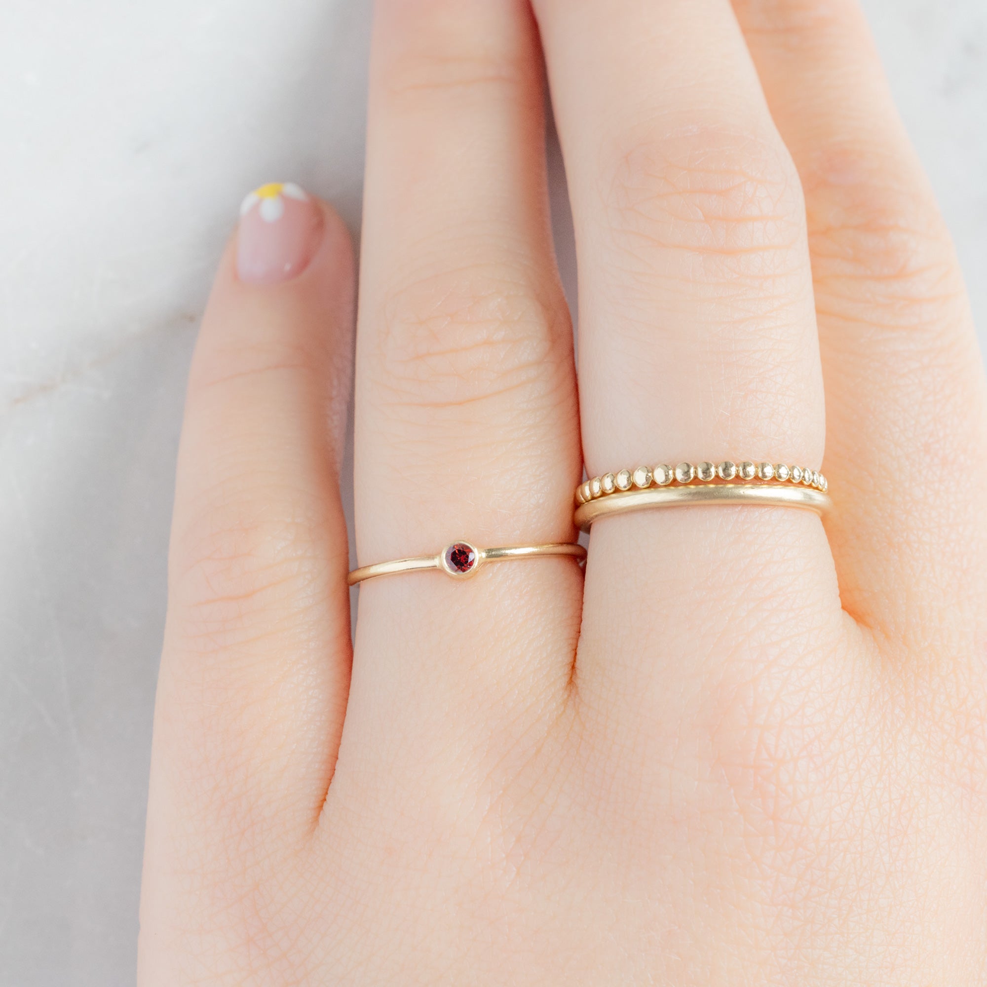 Custom Garnet Birthstone Stacking Ring | 10K Yellow Gold. Displayed on model's left hand ring finger alongside two other rings on consecutive finger.