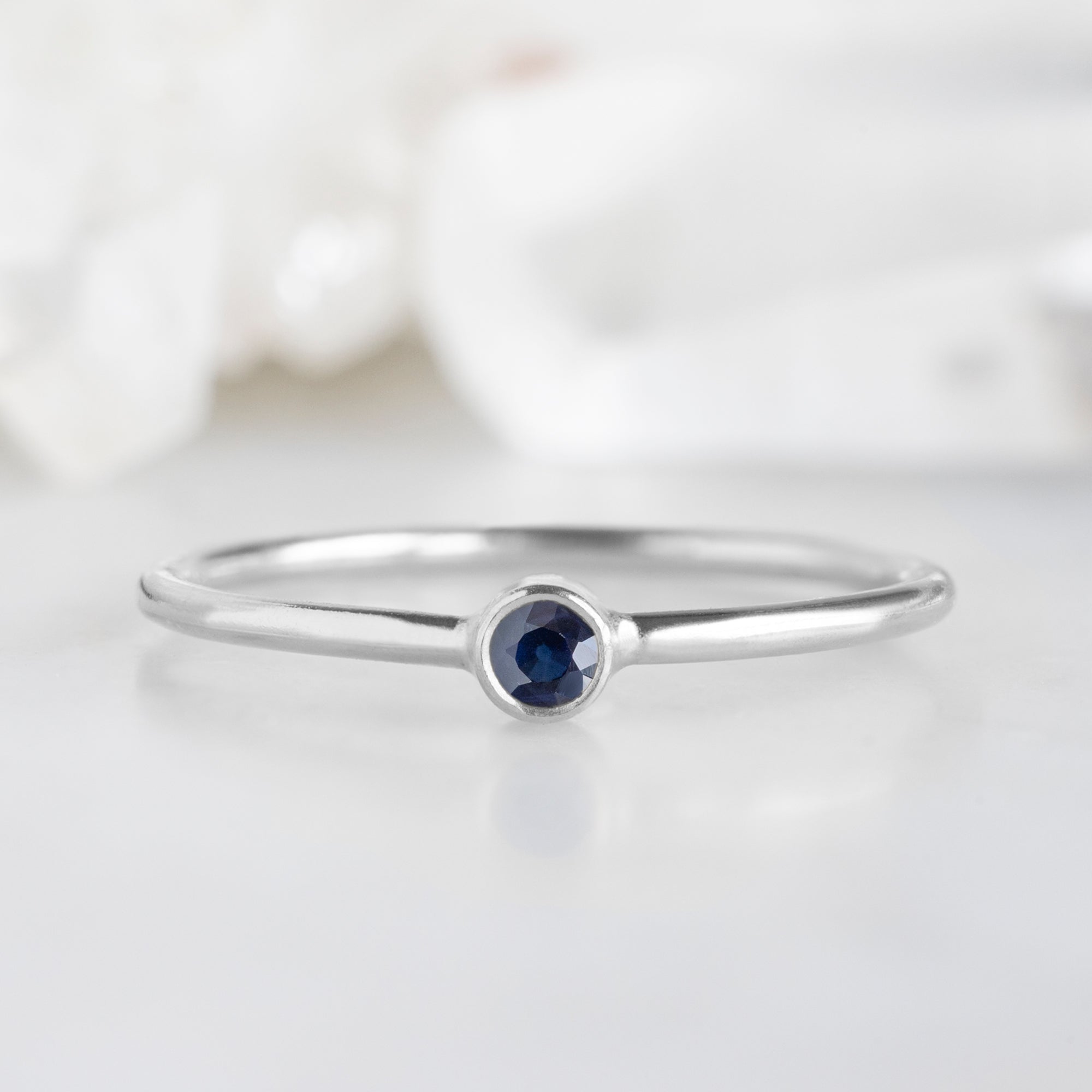 Custom Blue Sapphire Birthstone Stacking Ring | 10K White Gold displayed on marble surface with white blurred background.