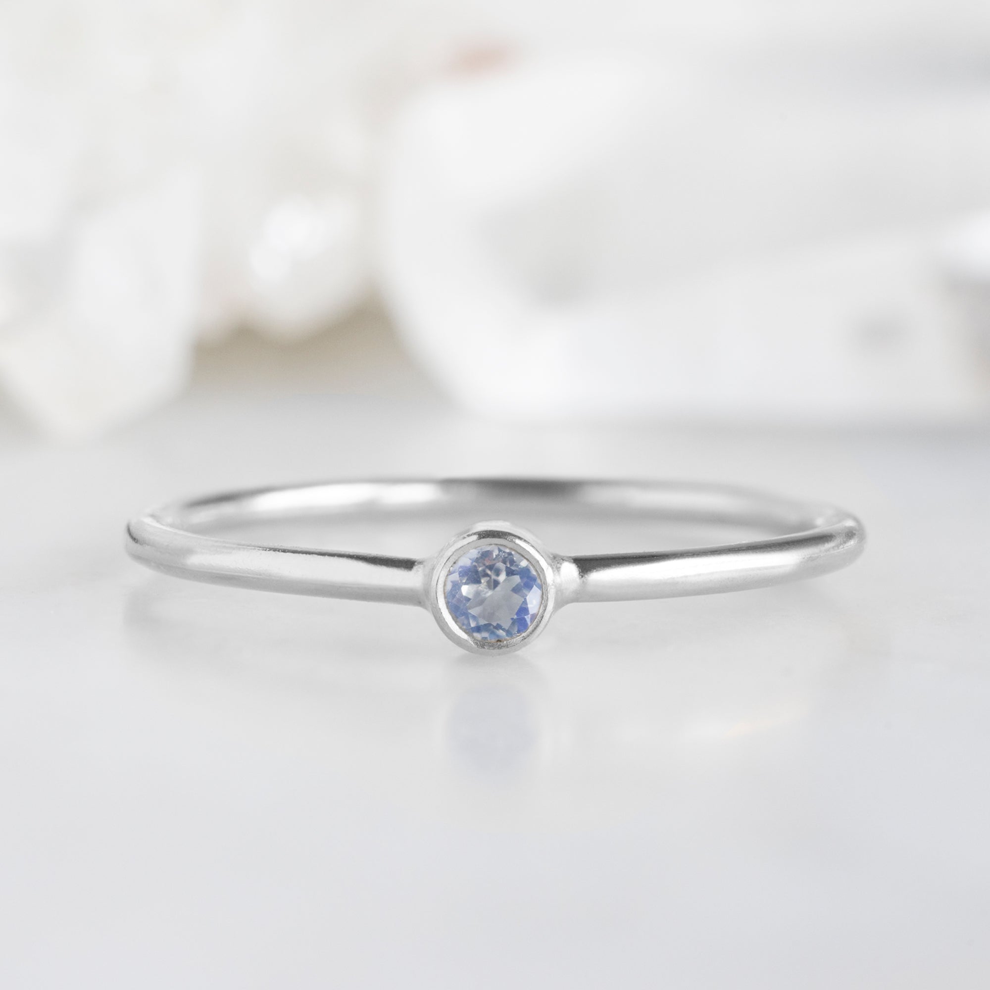 Custom Moonstone Birthstone Stacking Ring | 10K White Gold with blurred background.