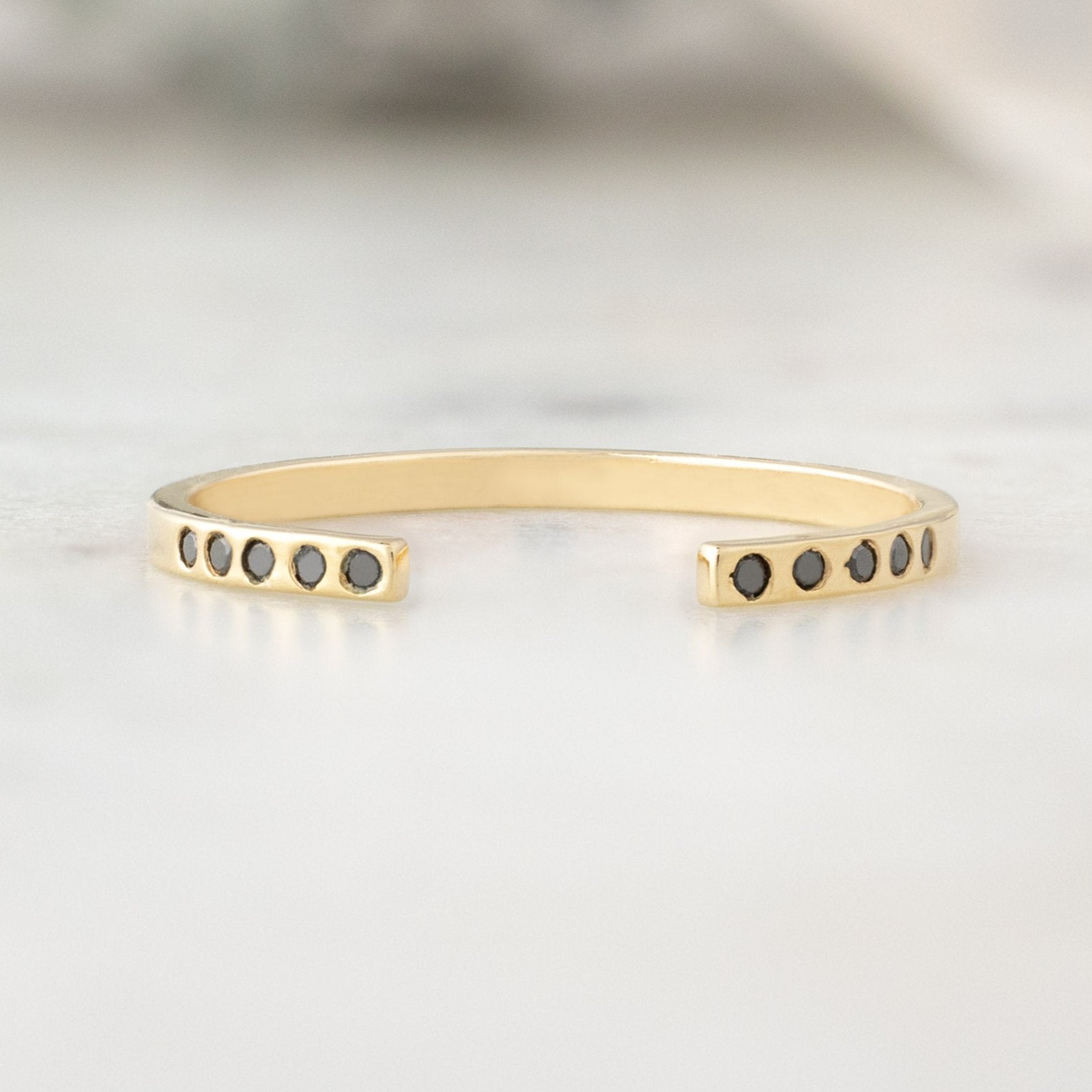 Open Cuff Flush Set Black Diamond Pavé Stacking Band in 14K Yellow Gold on White Marble Surface