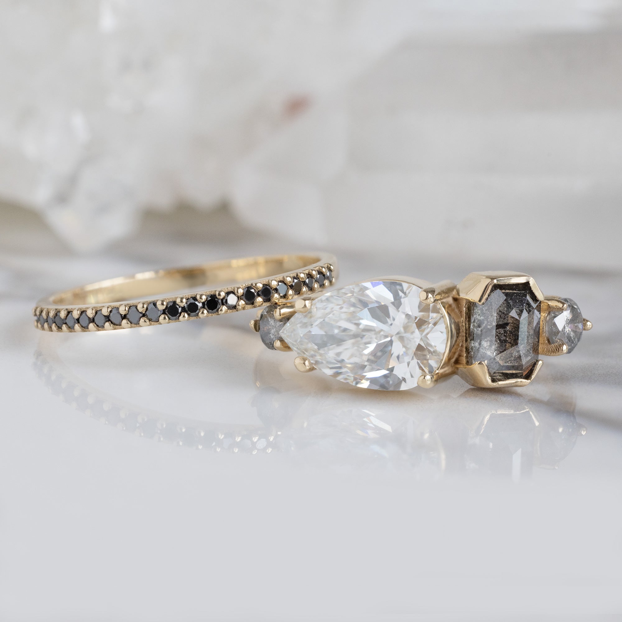 The Black Diamond Pavé Wedding Band in 14K Yellow Gold Stacked with Multi Diamond Engagement Rng on White Marble Tile