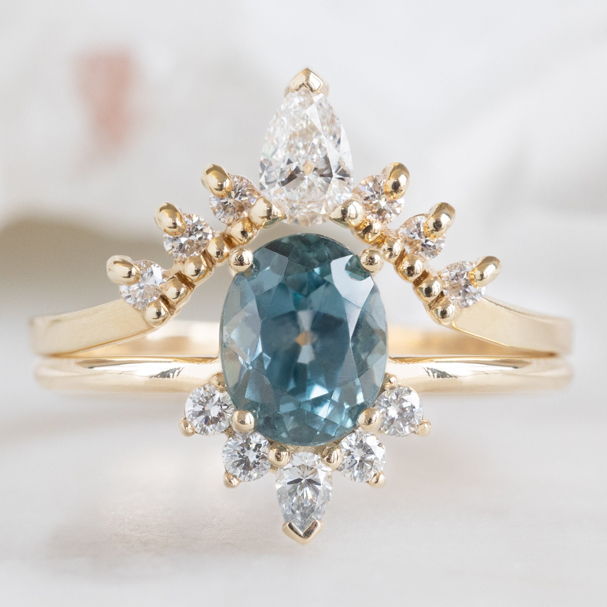 White Diamond Sunburst Stacking Band in 14K Yellow Gold Stacked with Oval Sapphire Gemstone Engagement Ring on White Marble Tile