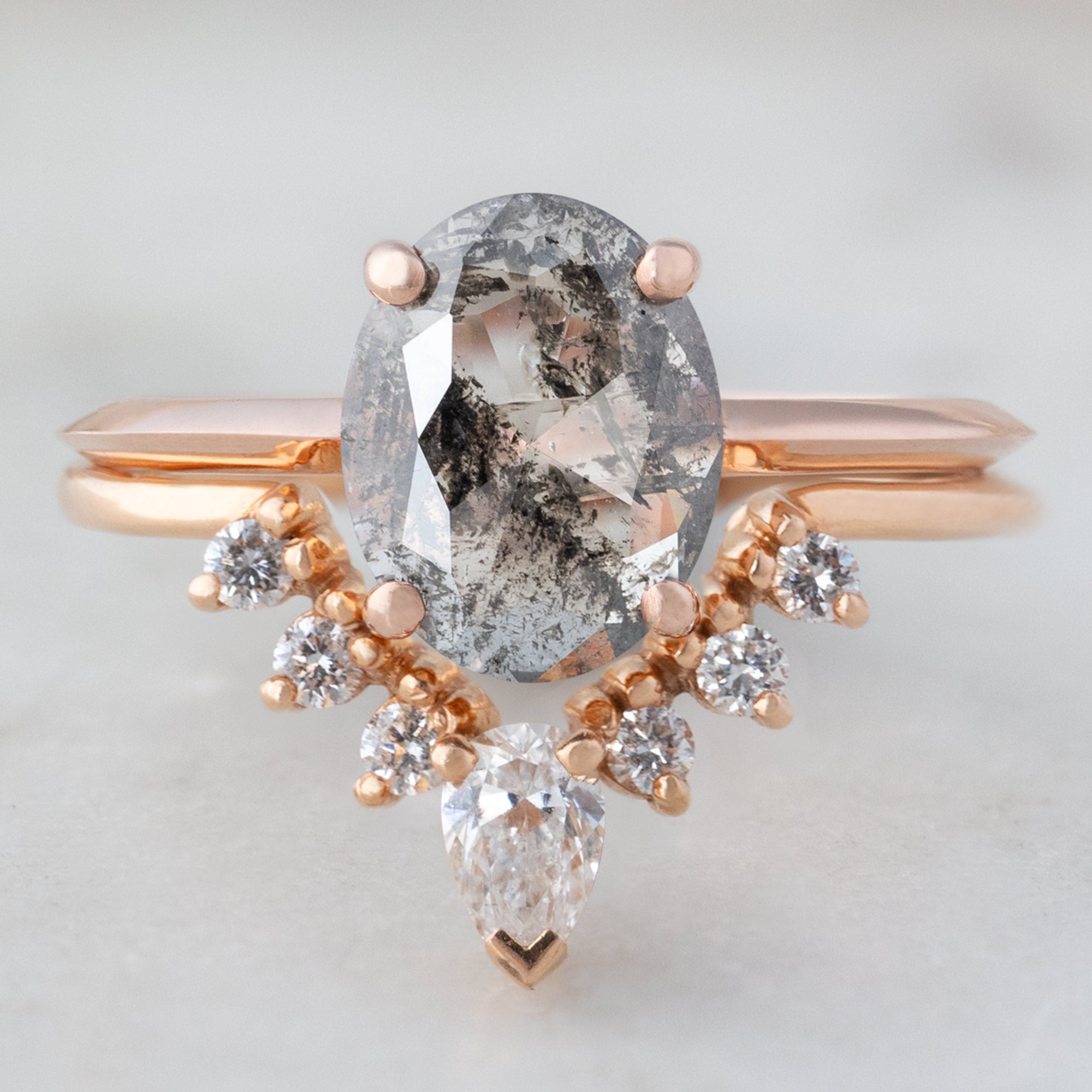 White Diamond Sunburst Stacking Band in 14K Rose Gold Stacked with Oval Salt and Pepper Diamond Engagement Ring on White Marble Tile