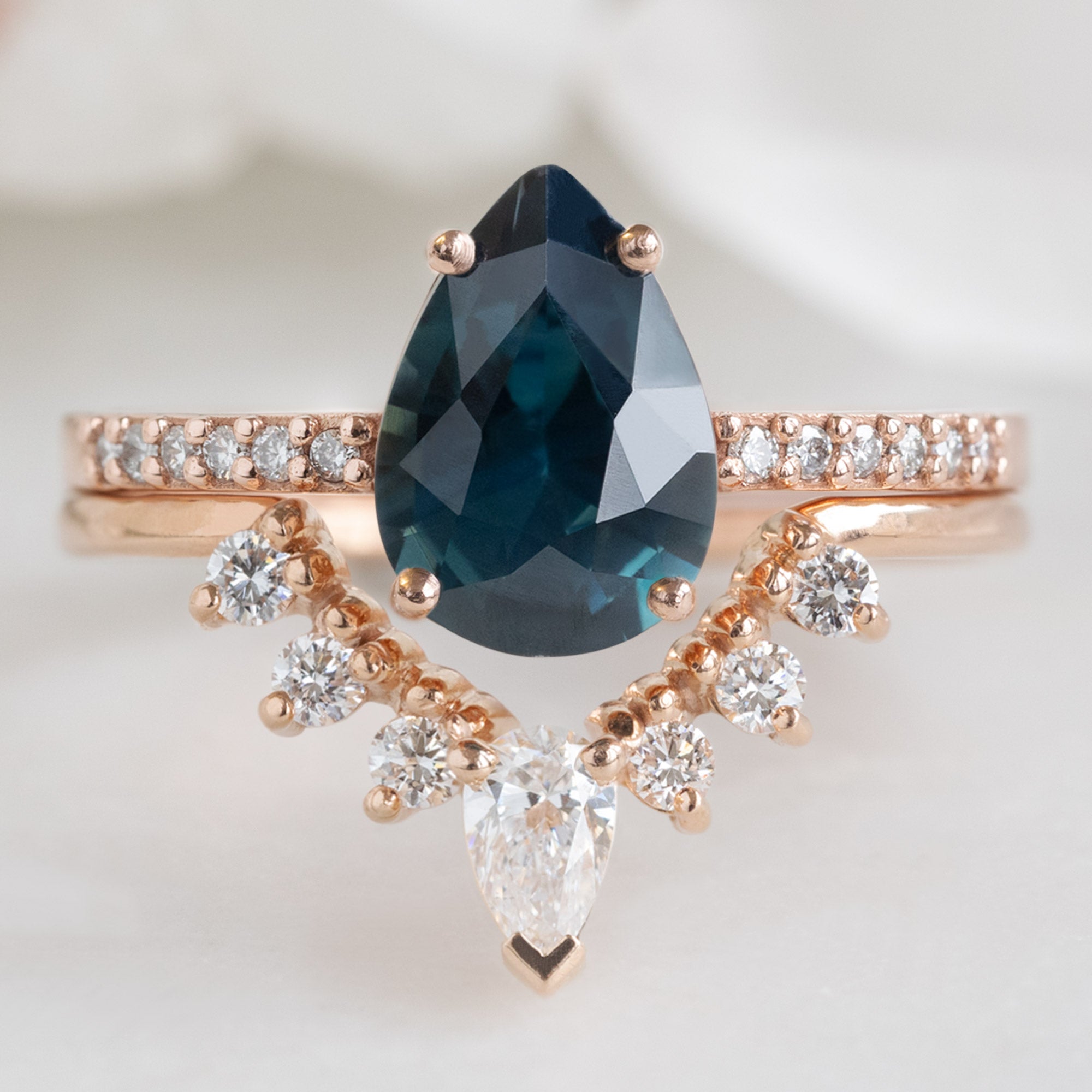 White Diamond Sunburst Stacking Band in 14K Rose Gold Stacked with Sapphire Pear Gemstone Engagement Ring on White Marble Tile